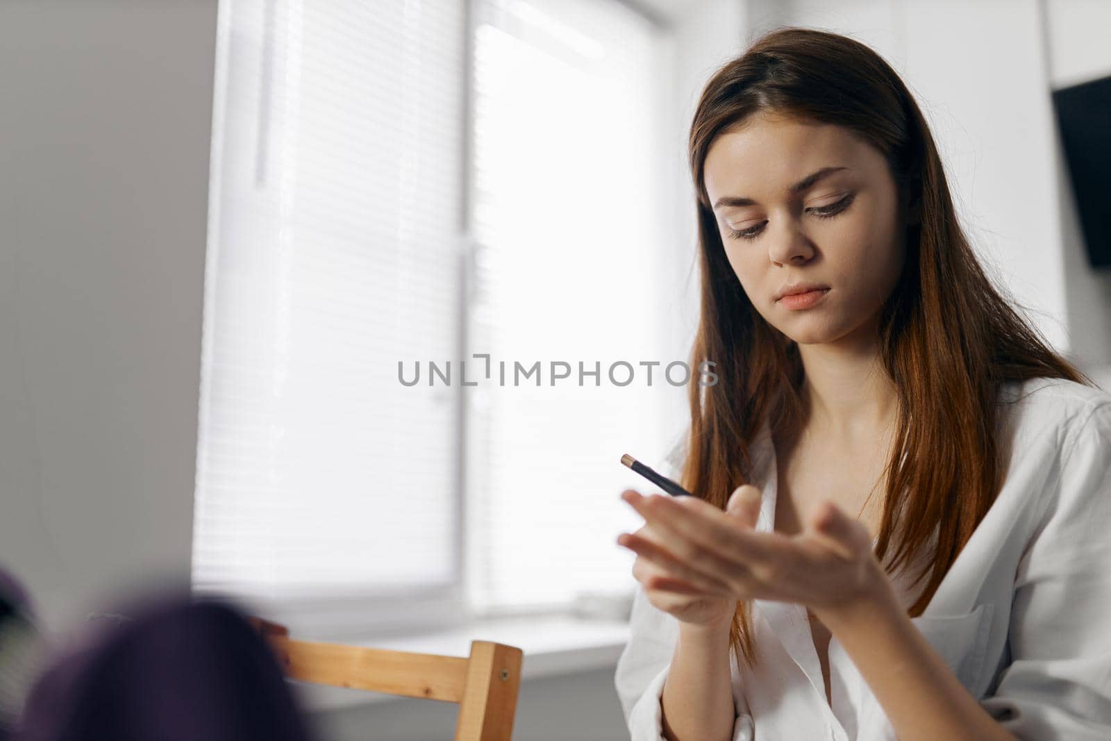 woman holding makeup pencil in hand indoors near window. High quality photo