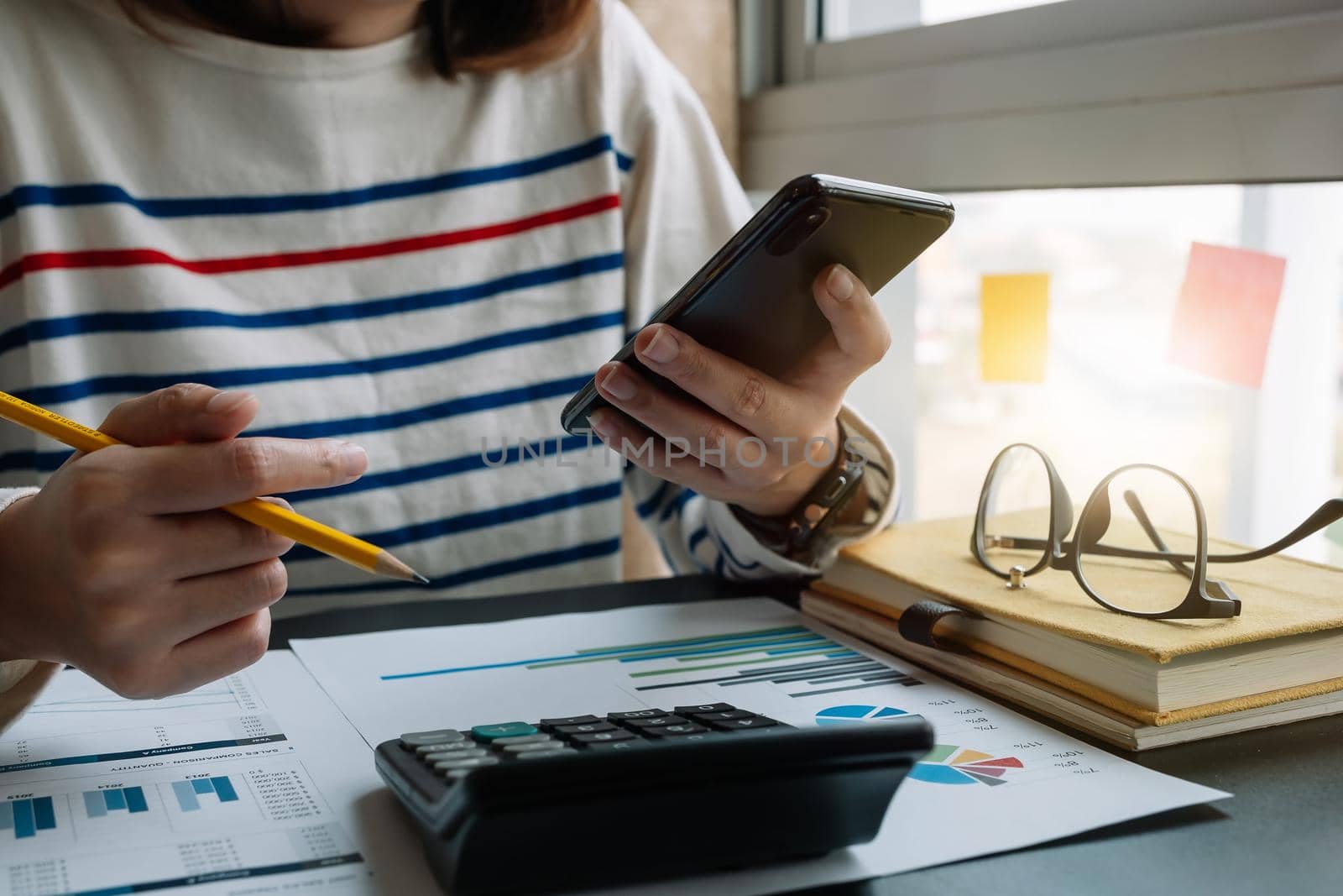 Close up of accountant hand holding smartphone while working on calculator to calculate financial data report, accountancy document and laptop computer at office, business work at home concept