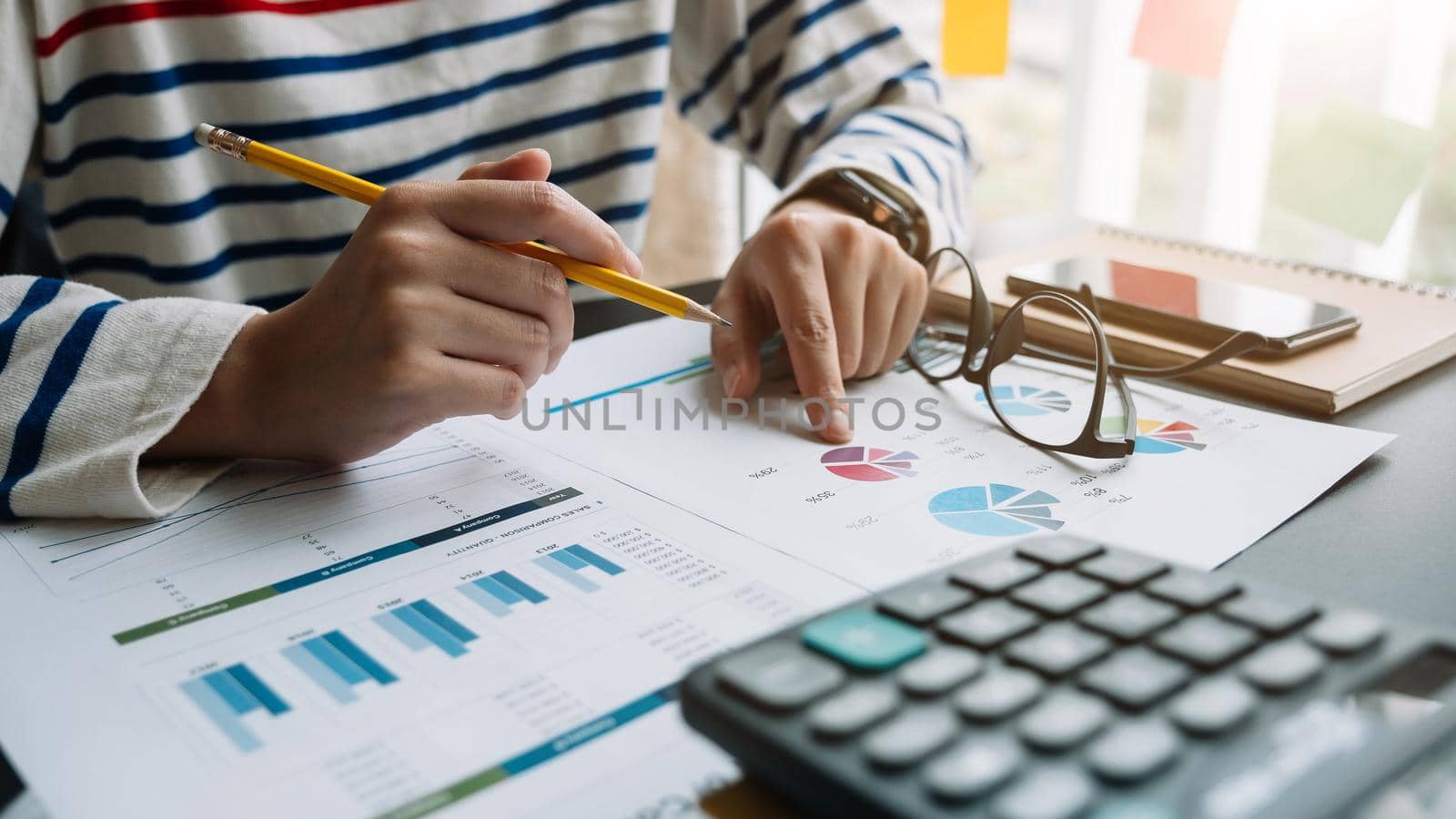 Close up of accountant hand holding pencil while working on calculator to calculate financial data report, accountancy document and laptop computer at office, business work at home concept