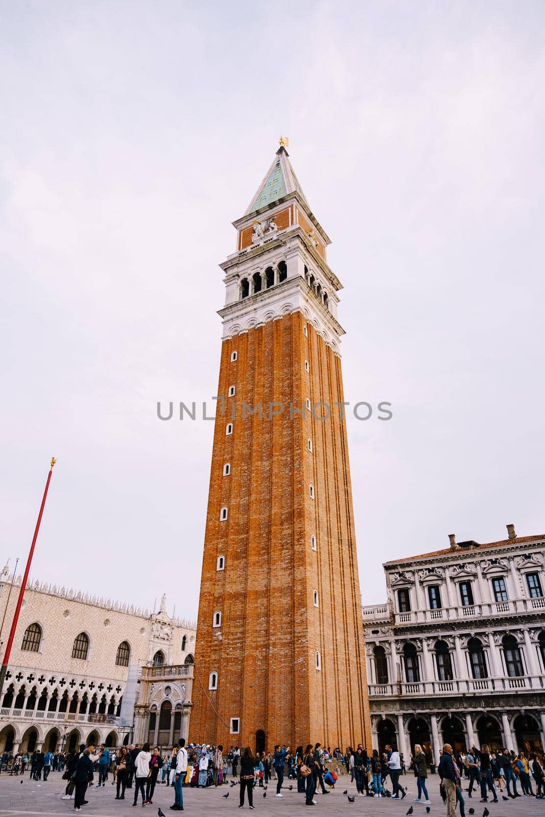 A huge bell tower made of red brick in Piazza San Marco in Venice, Italy. Against background of a cloudy, evening, October sunset sky.
