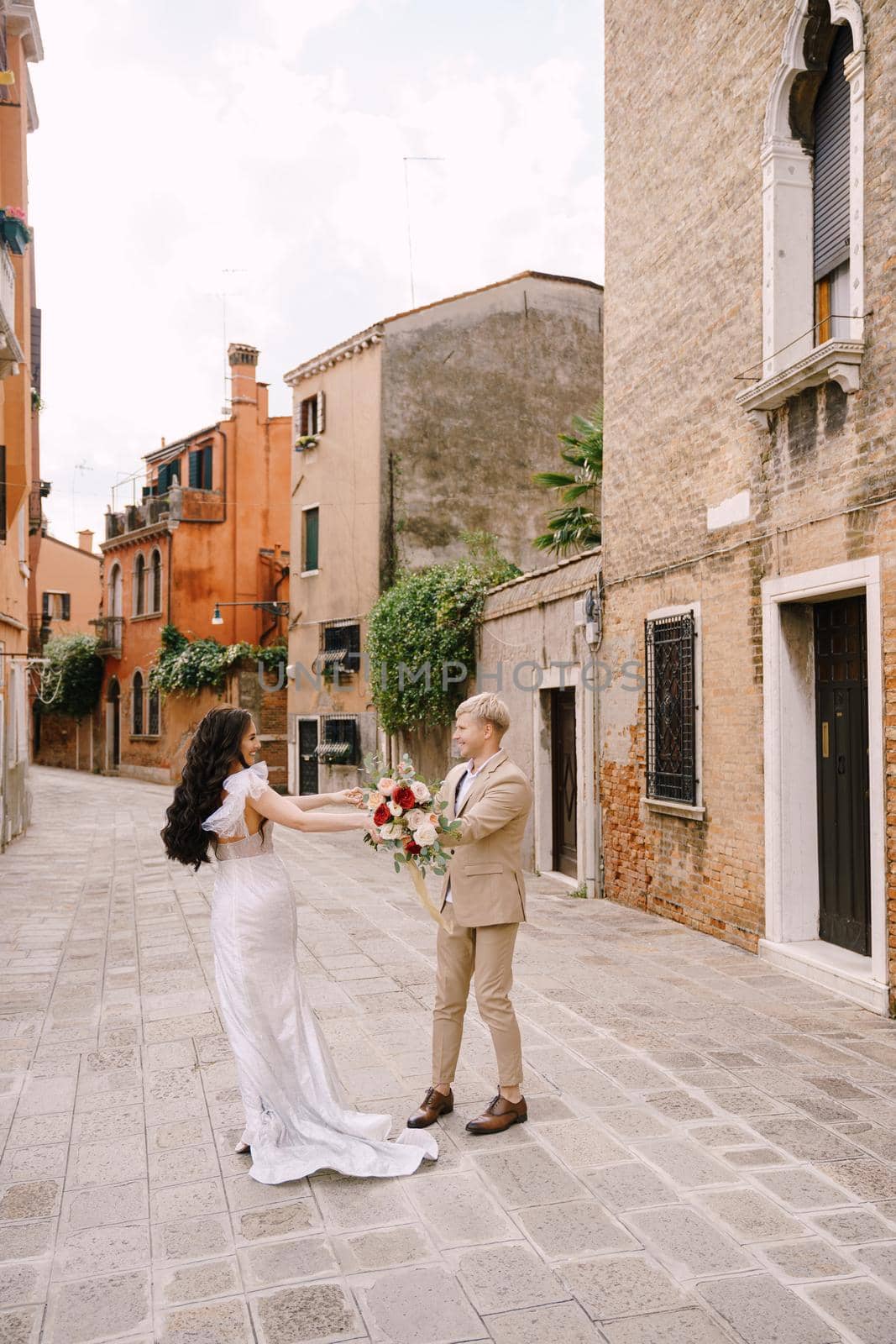 The bride and groom walk through the deserted streets of the city. Newlyweds hug, dance, hold hands against the backdrop of picturesque red brick houses.