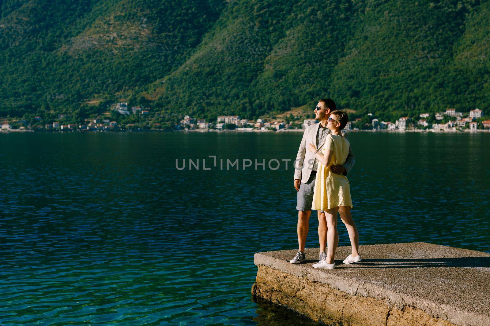A couple in love stands hugging on a pier in the Bay of Kotor near Perast against the backdrop of green slopes . High quality photo