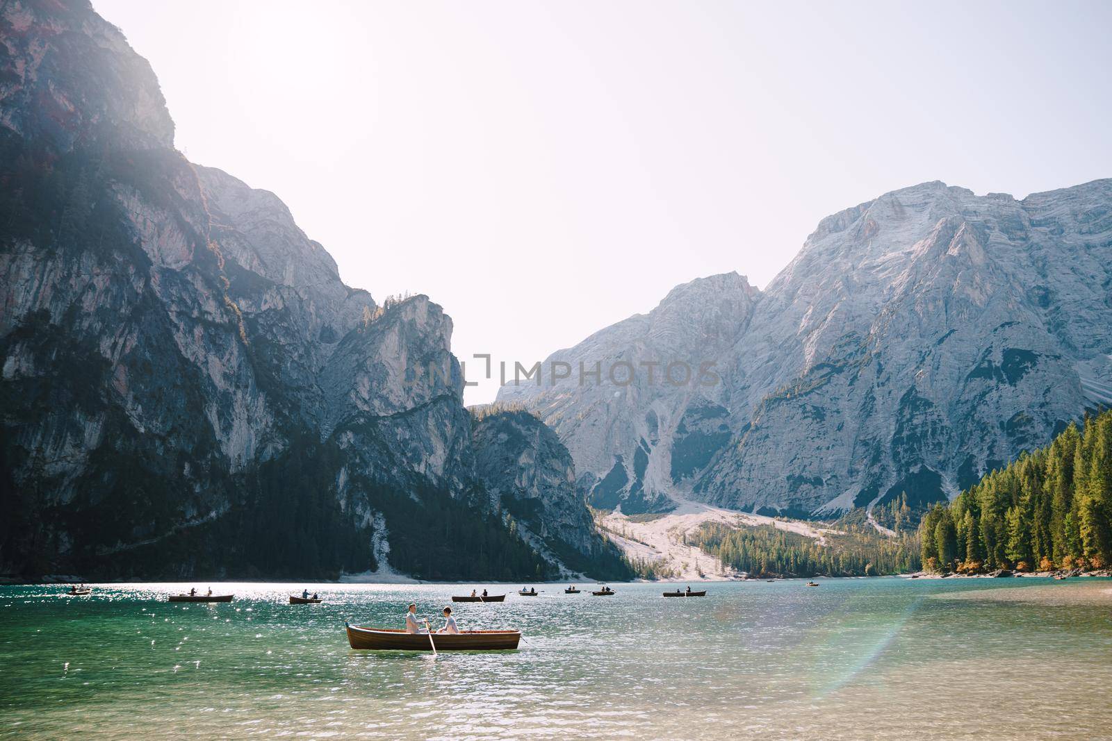 Newlyweds swim in a wooden boat on Lago di Braies in Italy. Wedding in Europe, at Braies lake. Wedding couple - Groom rows wooden oars, the bride sits opposite.