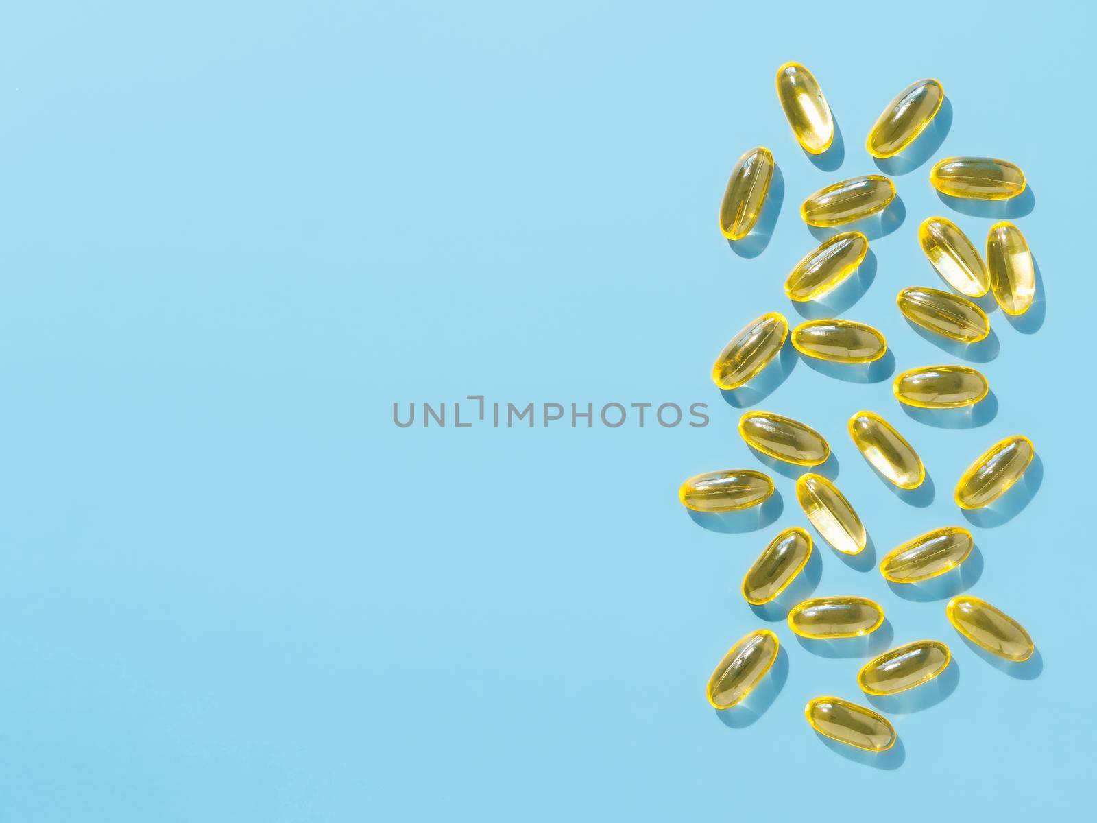 Vitamin D3, Omega or Evening Primrose Oil gel capsules on blue background. Top view or flat lay yellow liquid capsules with nutritional supplement oil. Copy space for text.