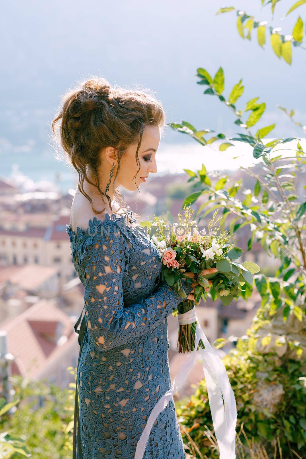 A bride in a blue dress stands with a bouquet in her hands, behind her opens a view of the old town of Kotor . High quality photo