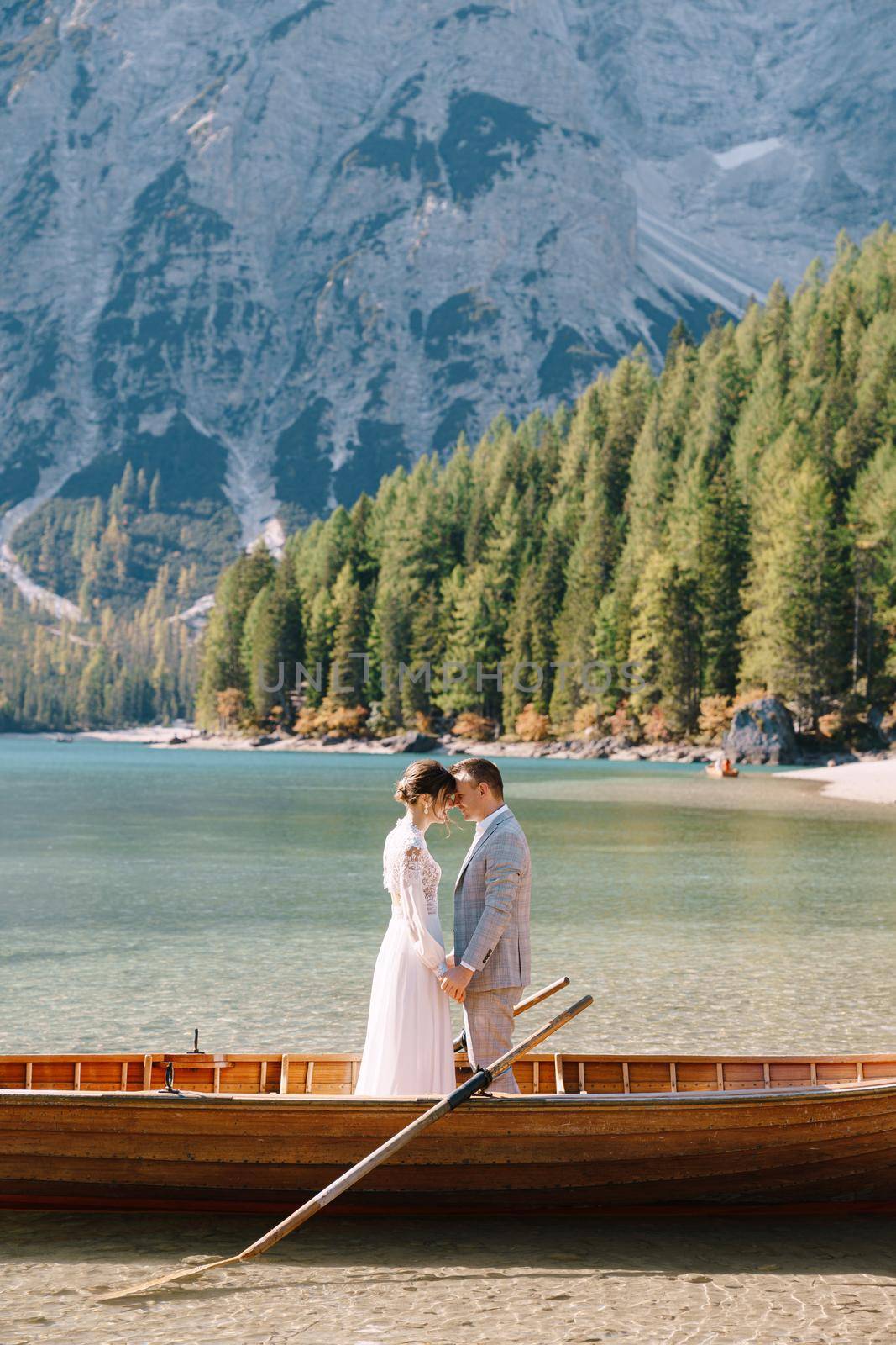 Bride and groom in a wooden boat at the Lago di Braies in Italy. Wedding couple in Europe, on Braies lake, in the Dolomites. The newlyweds are standing in the boat and hugging. by Nadtochiy