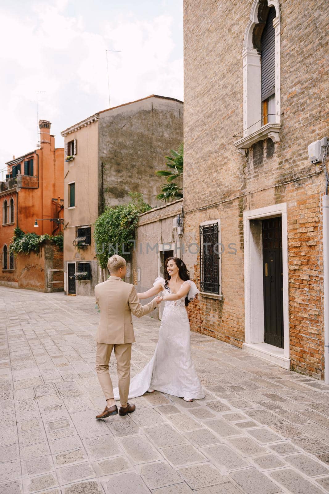 The bride and groom walk through the deserted streets of the city. Newlyweds hug, dance, hold hands against the backdrop of picturesque red brick houses.