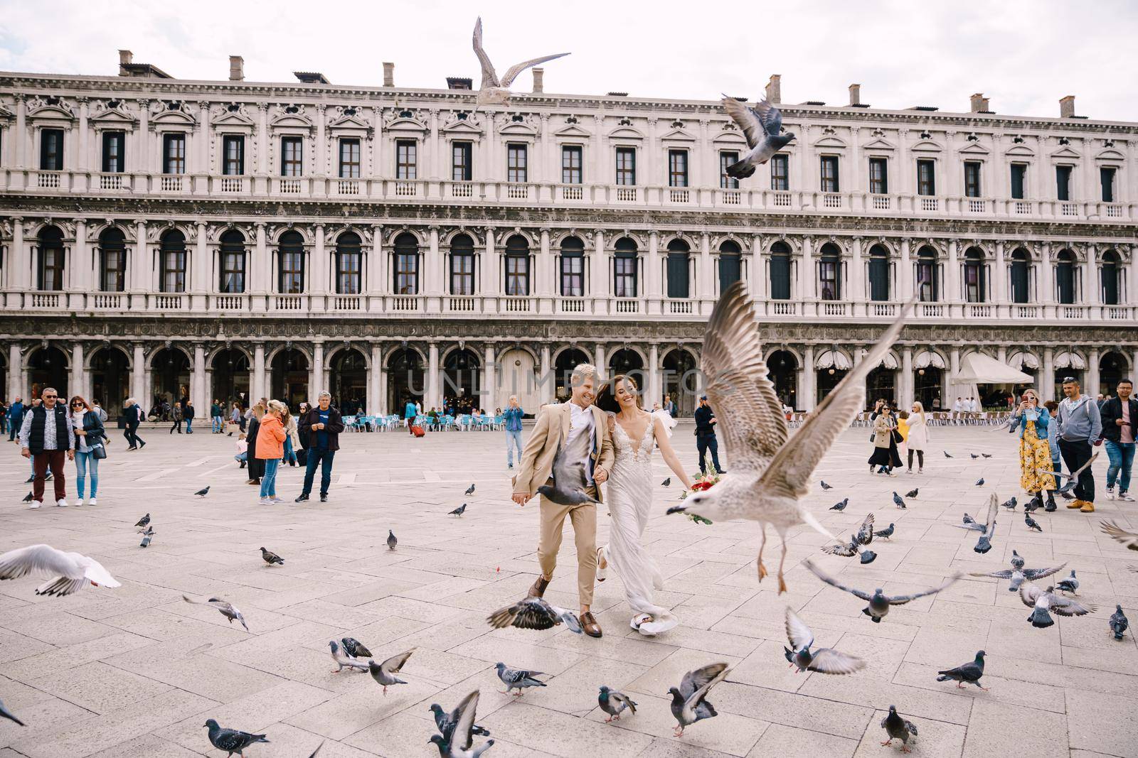 Venice, Italy - 04 october 2019: Venice Wedding, Italy. The bride and groom are running through a flock of flying pigeons in Piazza San Marco, amid the National Archaeological Museum Venice by Nadtochiy