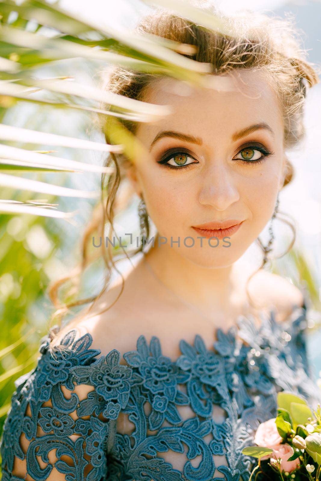 Portrait of a bride in a stylish blue dress with a bouquet in her hands near the green branches of a treeclose-up . High quality photo