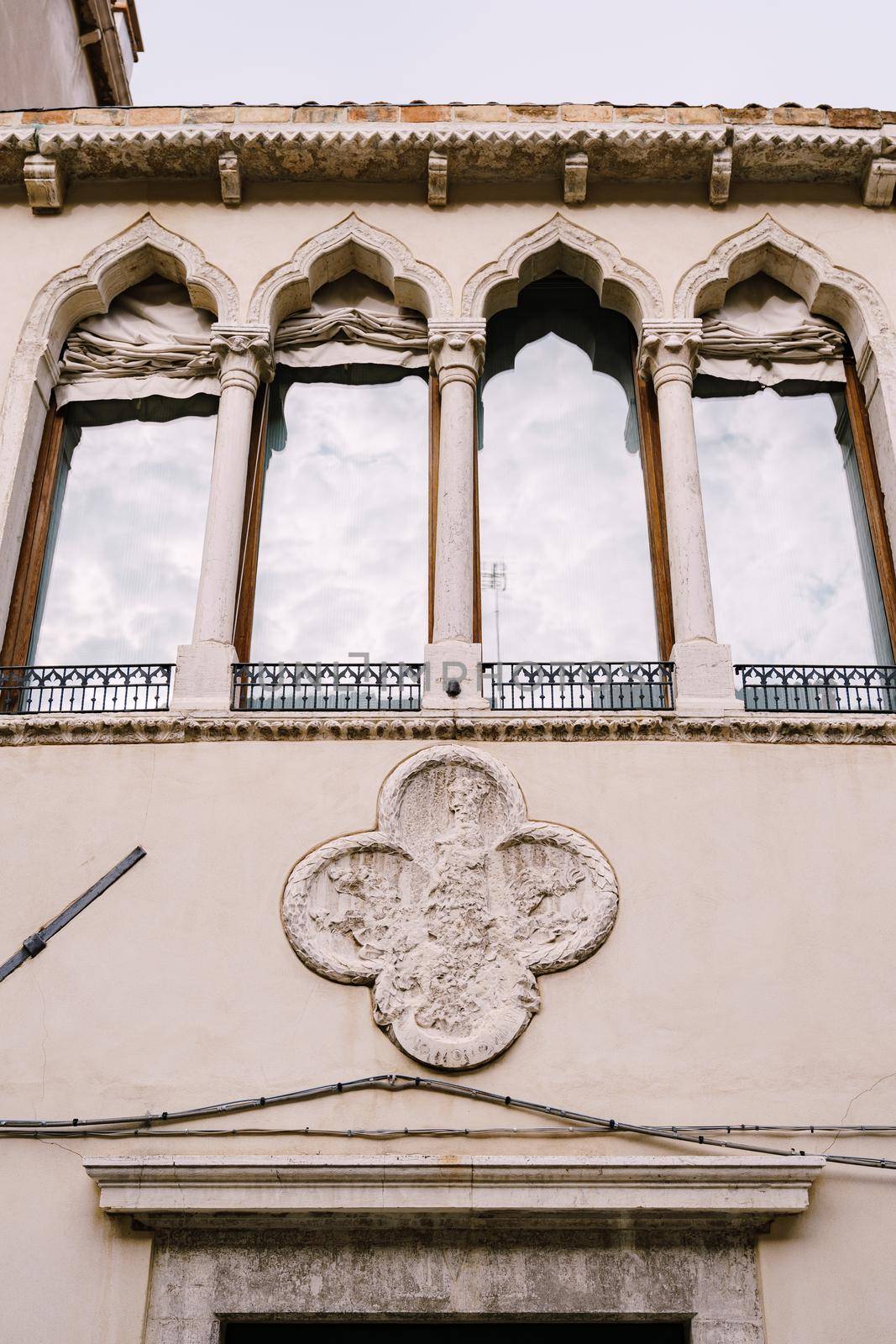Four Venetian windows with a reflection of the sky in the glass. Windows with a sharp top, with rag rollers outside, small forged windowsills.