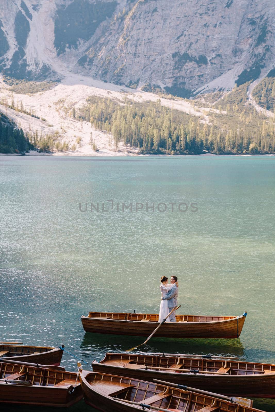 Bride and groom sailing in wooden boat, with oars at Lago di Braies lake in Italy. Wedding in Europe - Newlyweds are standing embracing in boat