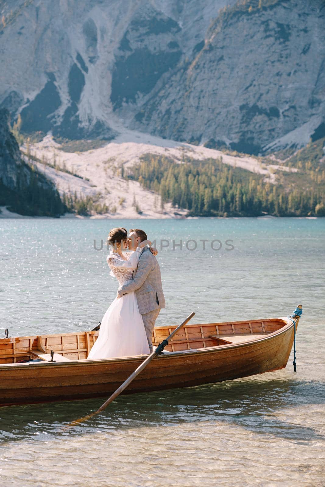 Bride and groom sailing in wooden boat, with oars at Lago di Braies lake in Italy. Wedding in Europe - Newlyweds are standing embracing in a boat. by Nadtochiy