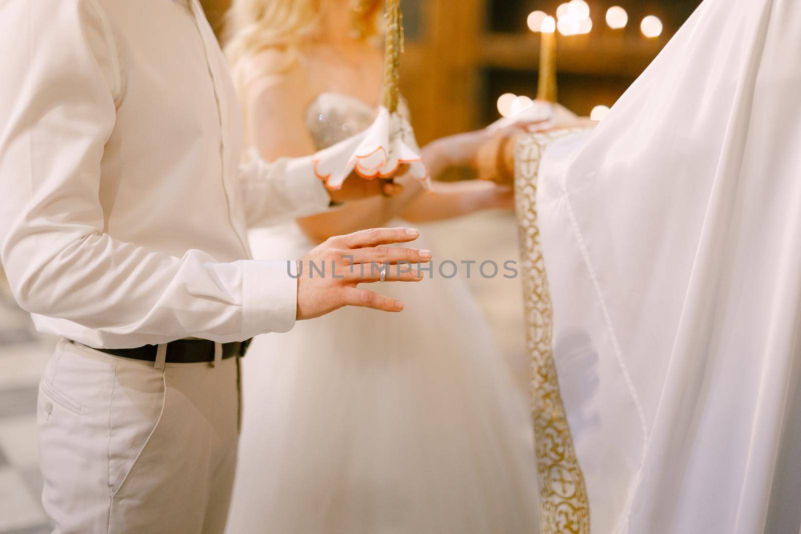 A priest in a white habit marrying the bride and groom in the church of St. Nicholas in Kotor by Nadtochiy