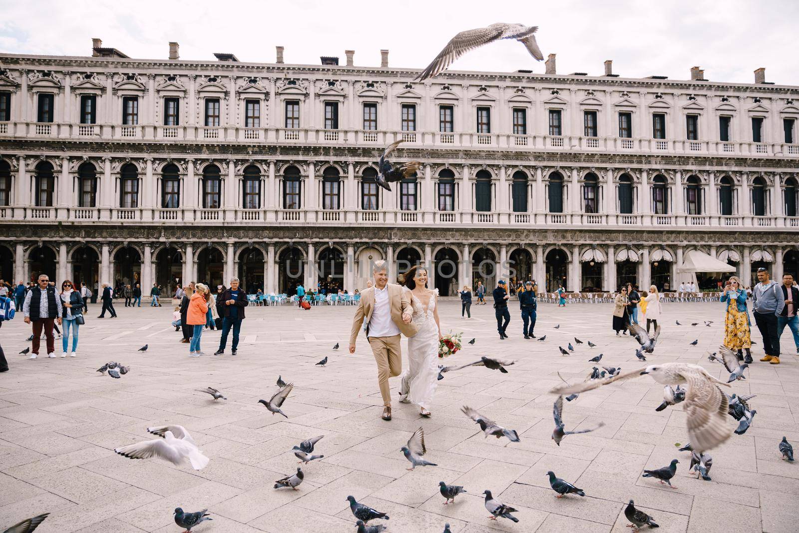 Venice, Italy - 04 october 2019: Venice Wedding, Italy. The bride and groom are running through a flock of flying pigeons in Piazza San Marco, amid the National Archaeological Museum Venice by Nadtochiy