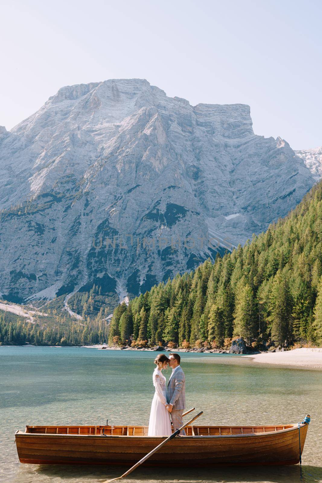 The bride and groom in a wooden boat at Lago di Braies in Italy. Wedding couple in Europe, at Braies lake. The newlyweds stand in the boat and cuddle.