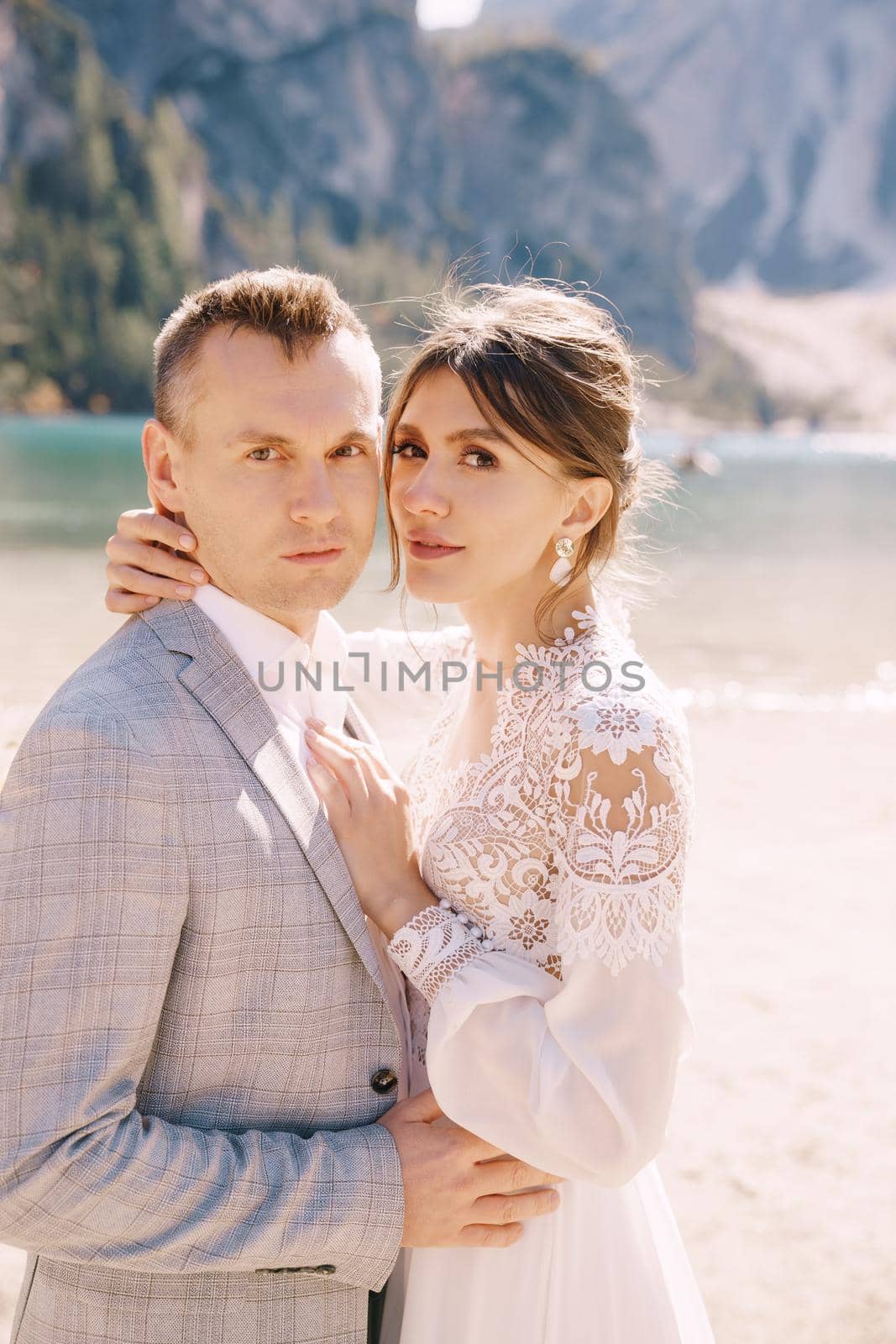 The bride and groom stand still for the ceremony, with an arch of autumn floral columns, against the backdrop of Lago di Braies in Italy. Destination wedding in Europe, at Braies lake.