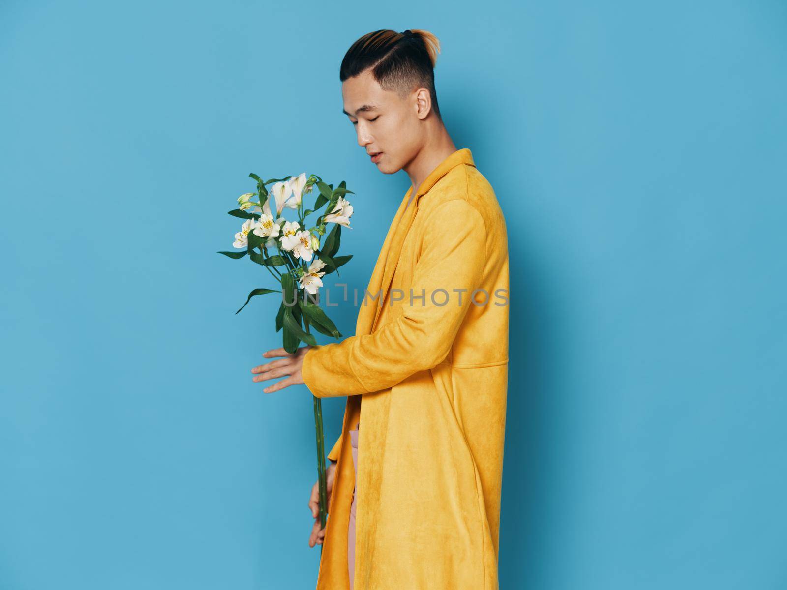 Side view of a man in a yellow coat with a bouquet of flowers on a blue background. High quality photo