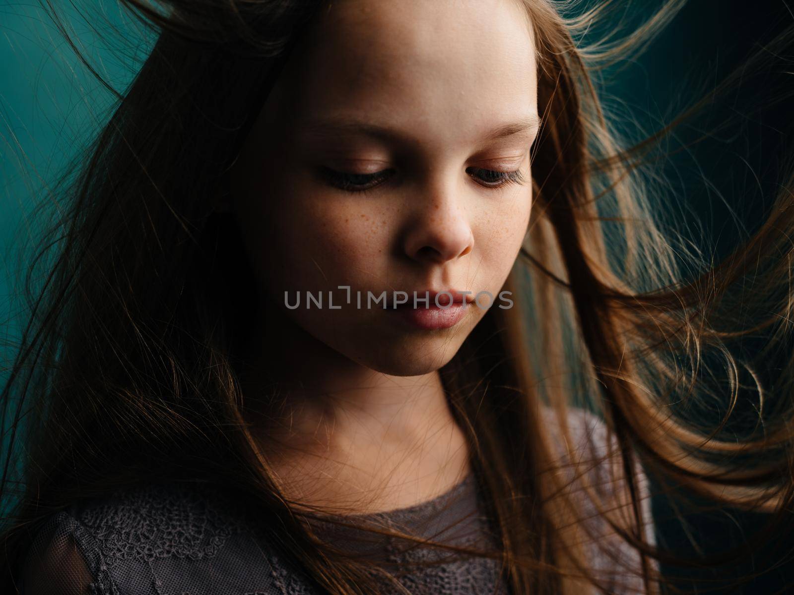 Sad girl with disheveled hair on a turquoise background in a gray dress. High quality photo