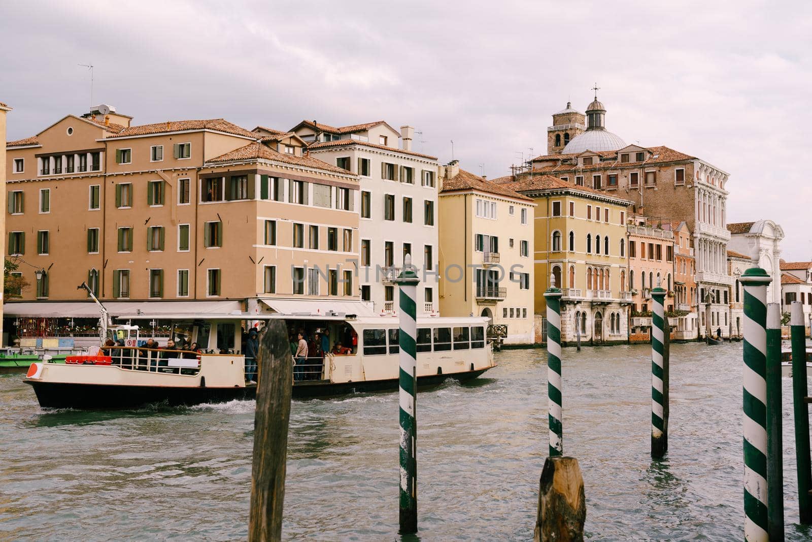 Tourists on the waterfront in Venice, against the background of the ancient facades of buildings standing in water. Water sightseeing in Venice, Italy.