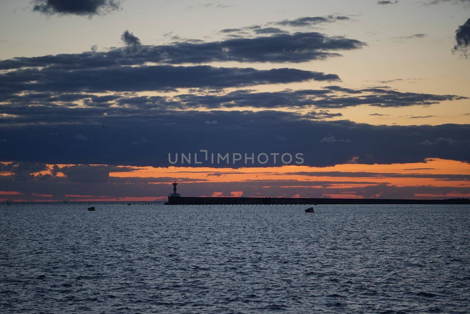 Sunset in the sea Bay on the payroll of the dark sky and Cape with a shining lighthouse