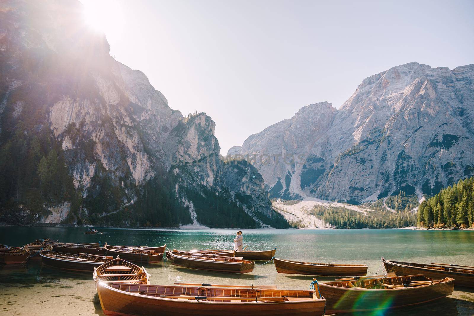 Bride and groom in a wooden boat at the Lago di Braies in Italy. Wedding couple in Europe, on Braies lake, in the Dolomites. The newlyweds are standing in the boat and hugging. by Nadtochiy