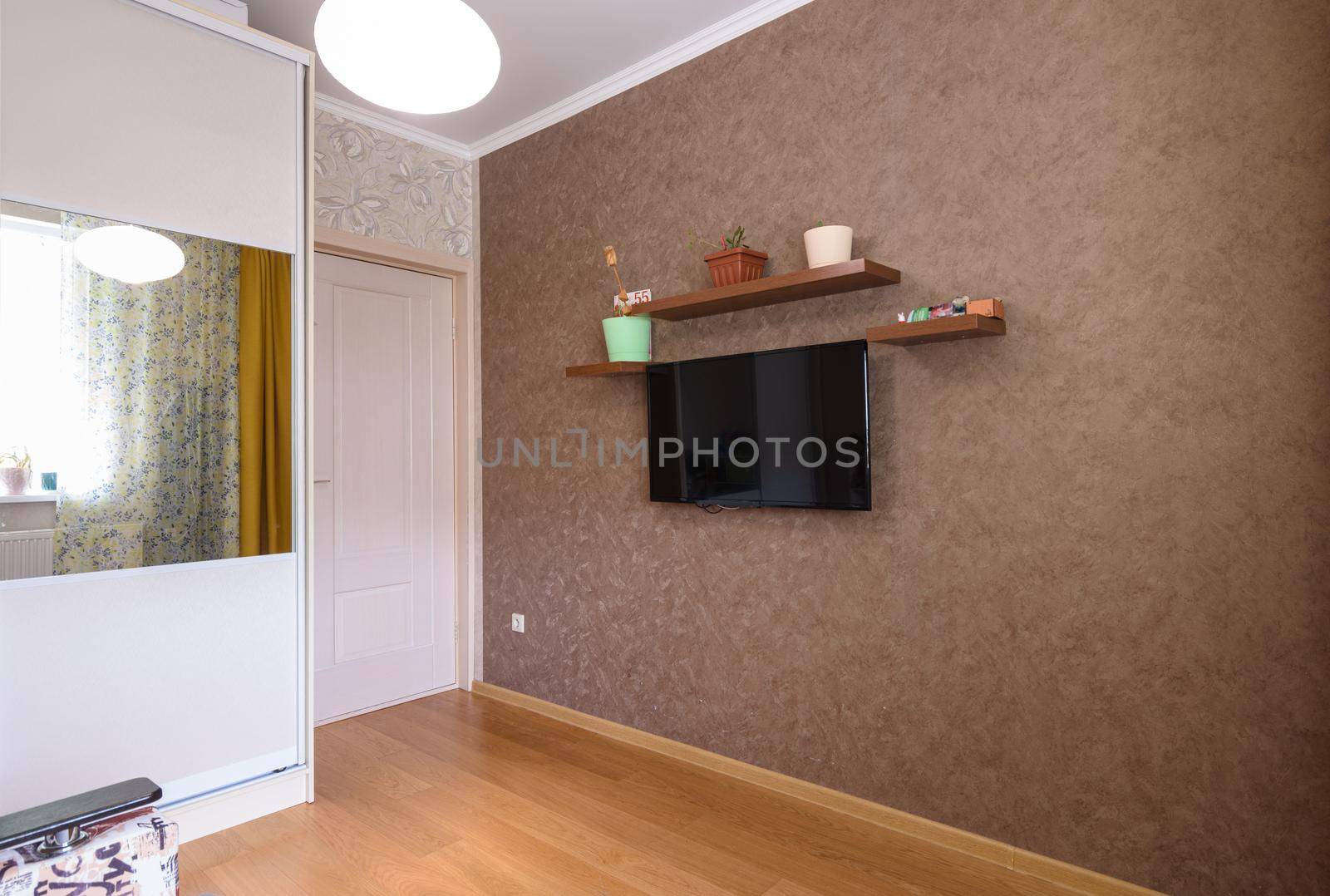 The interior of a small room, a view of the wardrobe, an entrance door and a wall with a TV and shelves