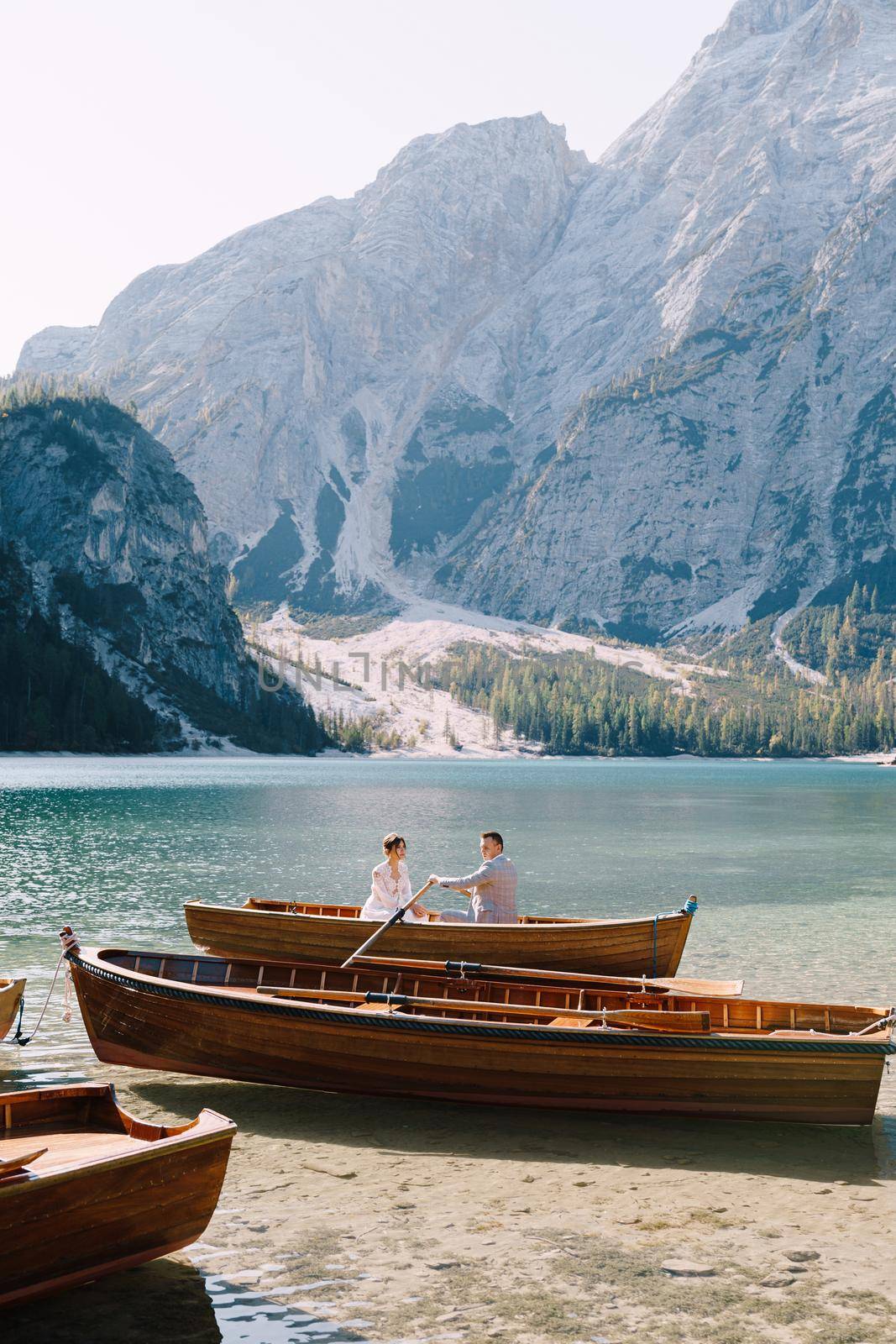 Newlyweds sail in a wooden boat on the Lago di Braies in Italy. Wedding in Europe, on Braies lake. Wedding couple - The groom rows with wooden oars, the bride sits opposite. by Nadtochiy