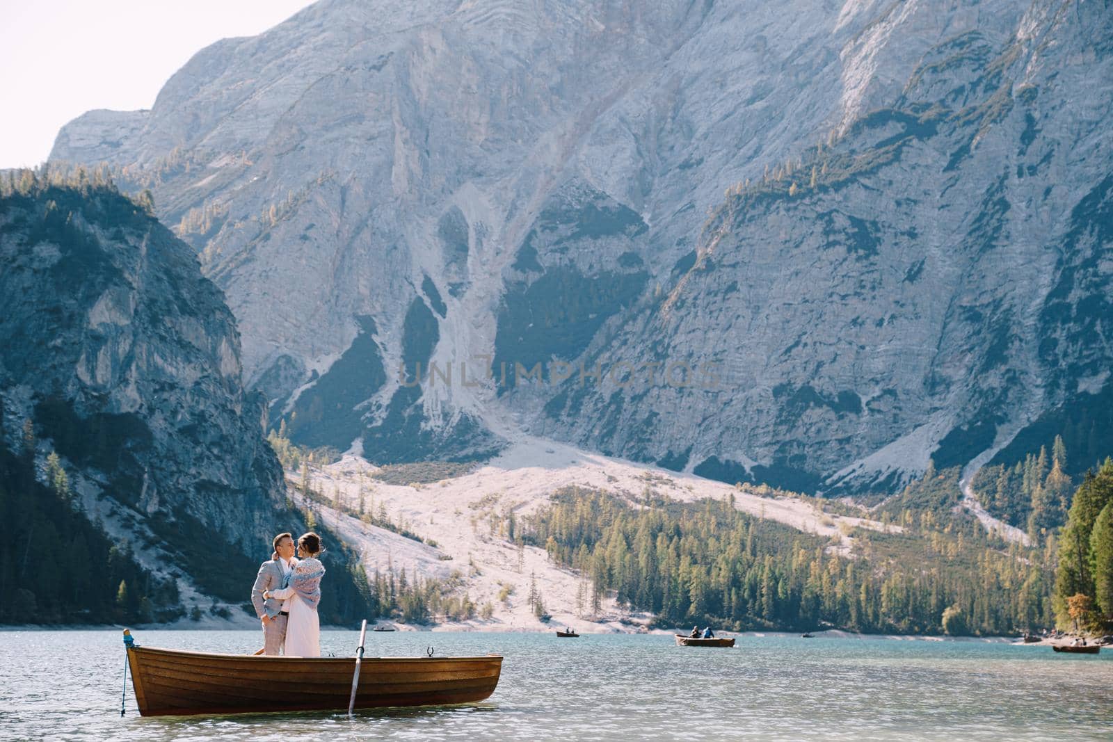 Bride and groom sailing in wooden boat, with oars at Lago di Braies lake in Italy. Wedding in Europe - Newlyweds are standing embracing in a boat. by Nadtochiy