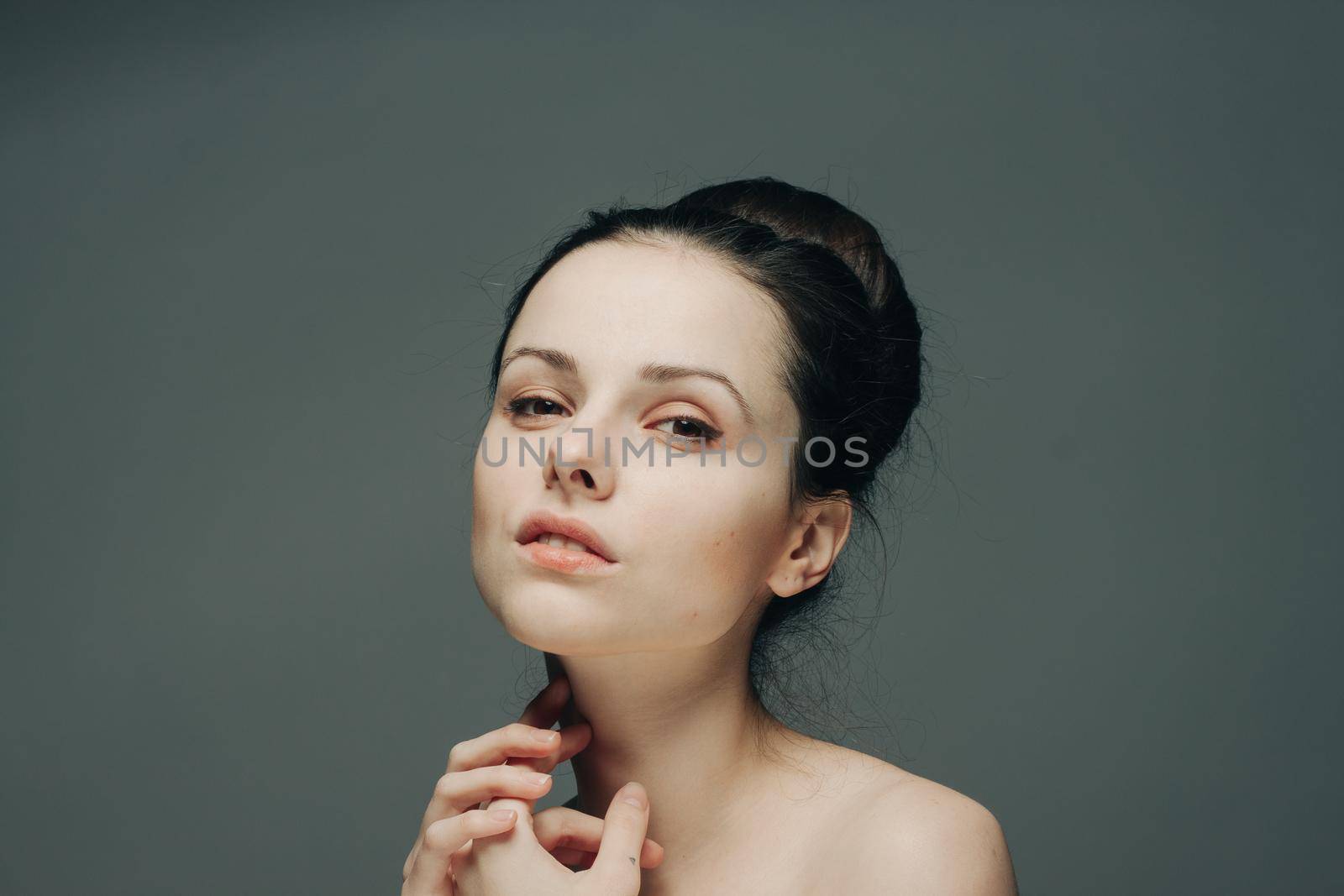 nude woman with hairstyles in her head touches her face with her hands on a gray background by SHOTPRIME