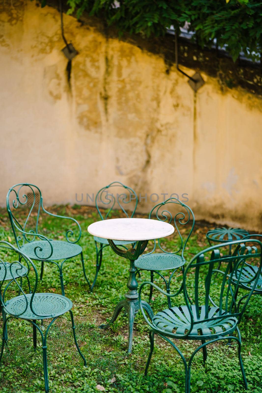 White small cocktail table surrounded by six green forged metal chairs in front of a cement wall at Medici Villa of Lilliano Wine Estate in Tuscany, Italy.