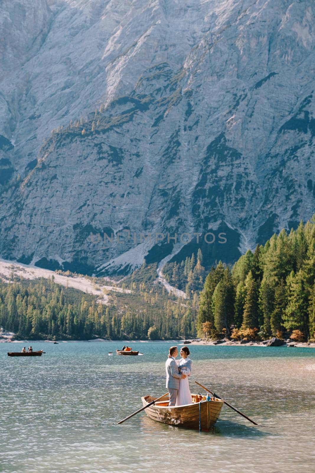 Bride and groom sailing in wooden boat, with oars at Lago di Braies lake in Italy. Wedding in Europe - Newlyweds are standing embracing in boat