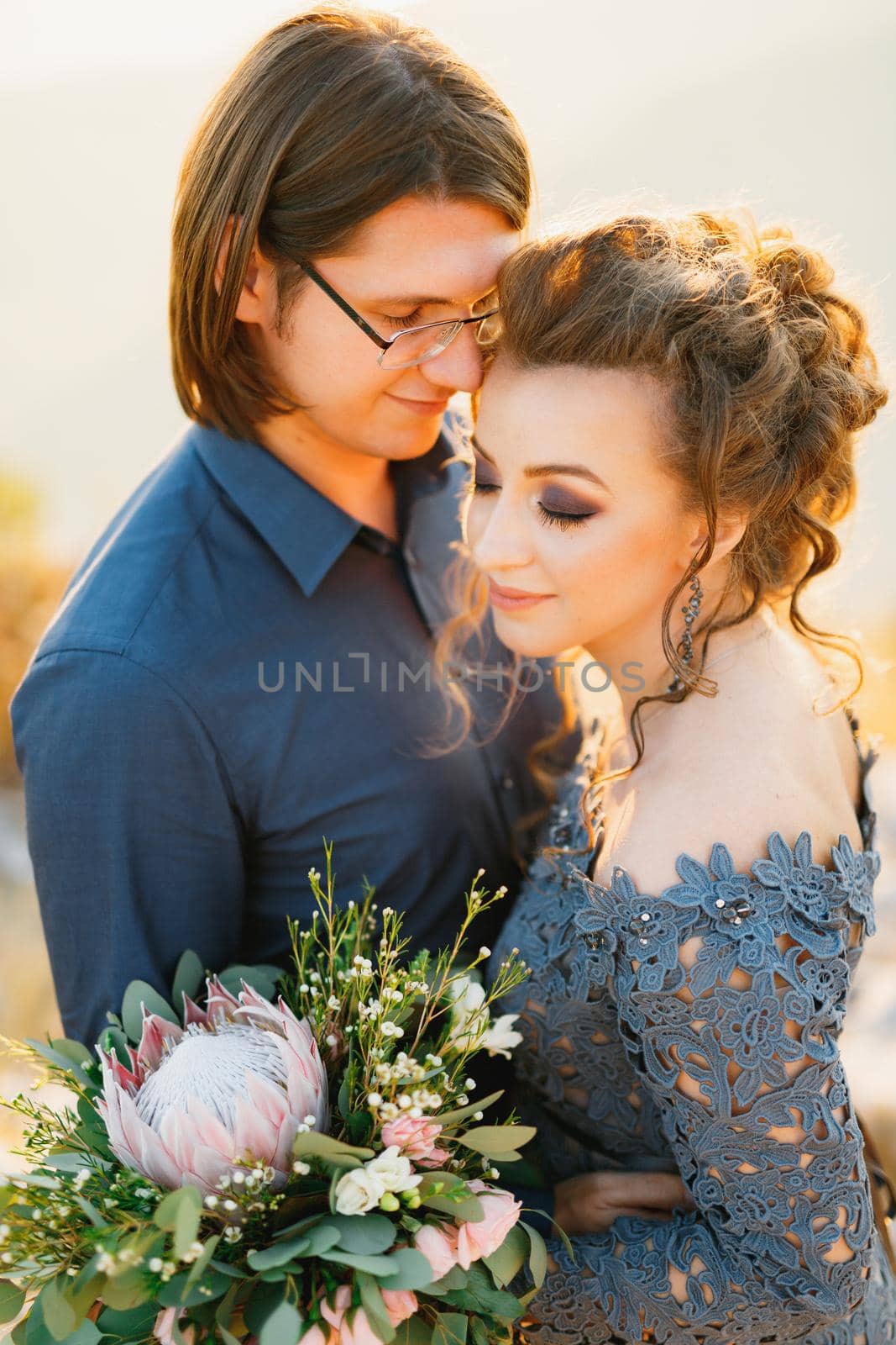 The bride and groom tenderly hug, the bride holds a bouquet with protea, eucalyptus and roses in her hands, close-up. High quality photo