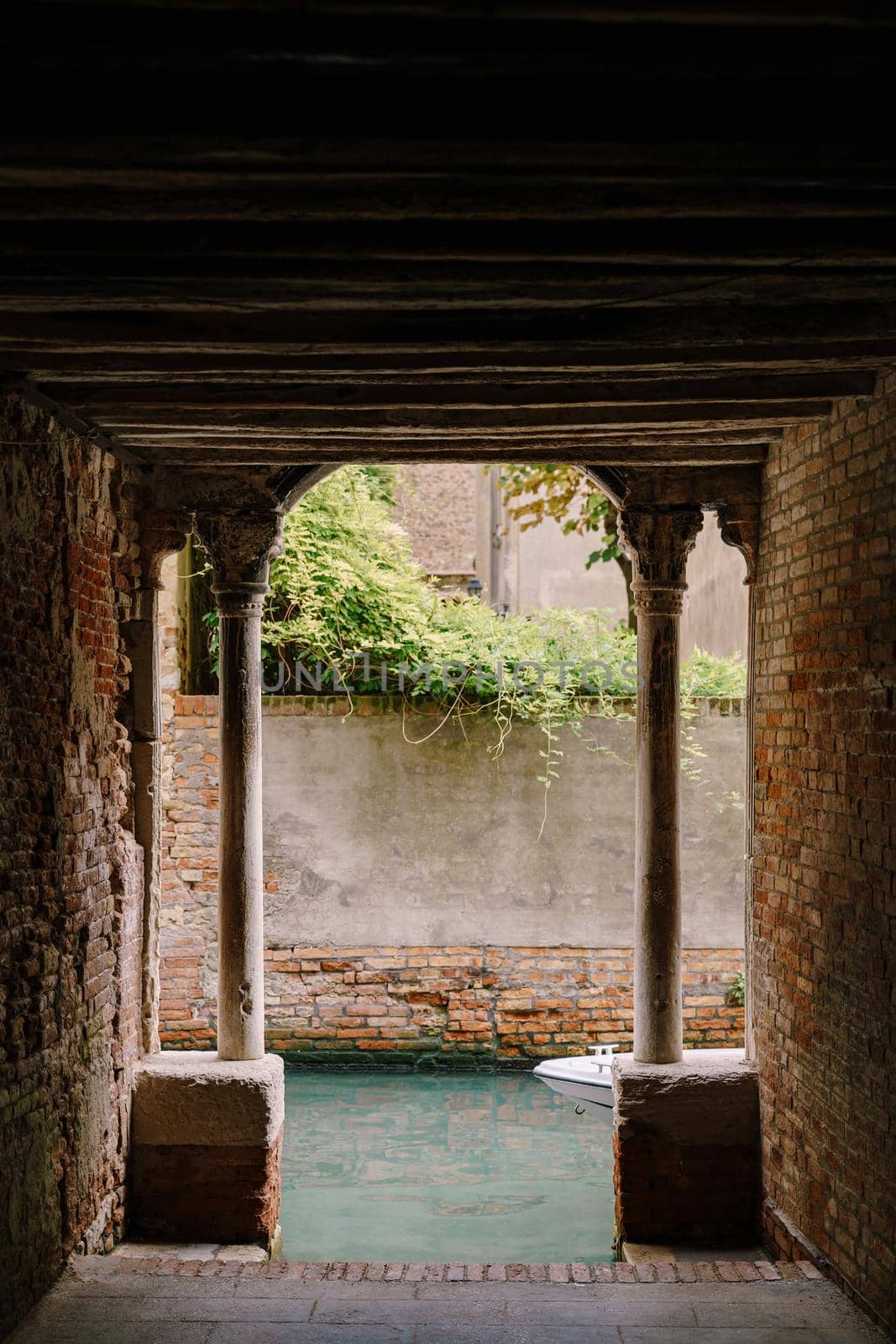 View from the building on to a small narrow canal between houses in Venice, Italy. A view from tunnel with brick walls, two antique columns and water in the sea.