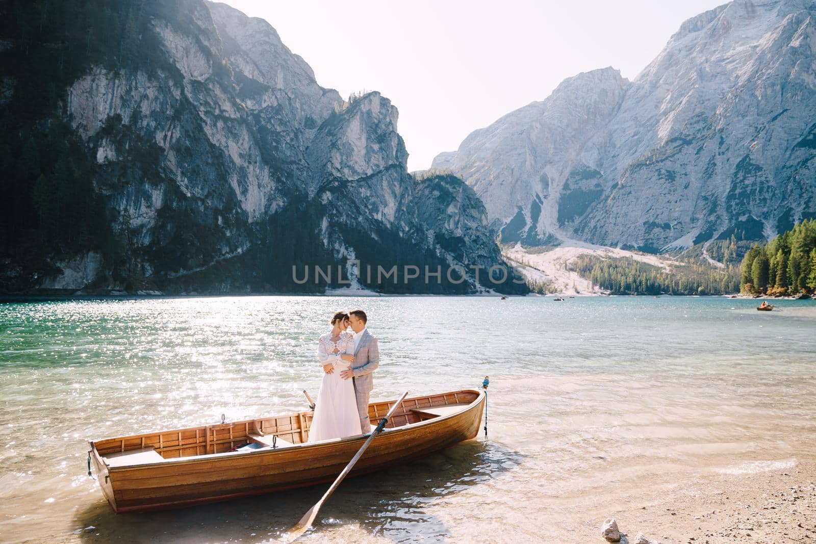 Bride and groom sailing in wooden boat, with oars at Lago di Braies lake in Italy. Wedding in Europe - Newlyweds are standing embracing in a boat. by Nadtochiy