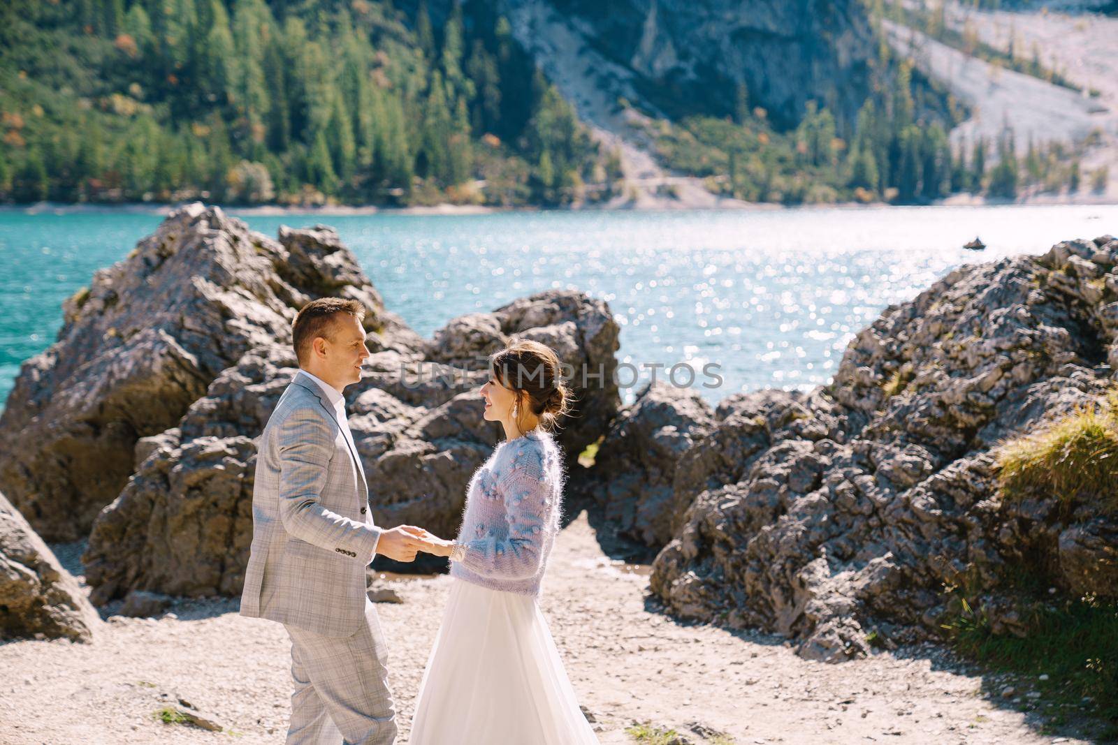 Bride and groom stand against the backdrop of stones overlooking Lago di Braies in Italy. Destination wedding in Europe, on Braies lake. Loving newlyweds walk against the backdrop of amazing nature. by Nadtochiy