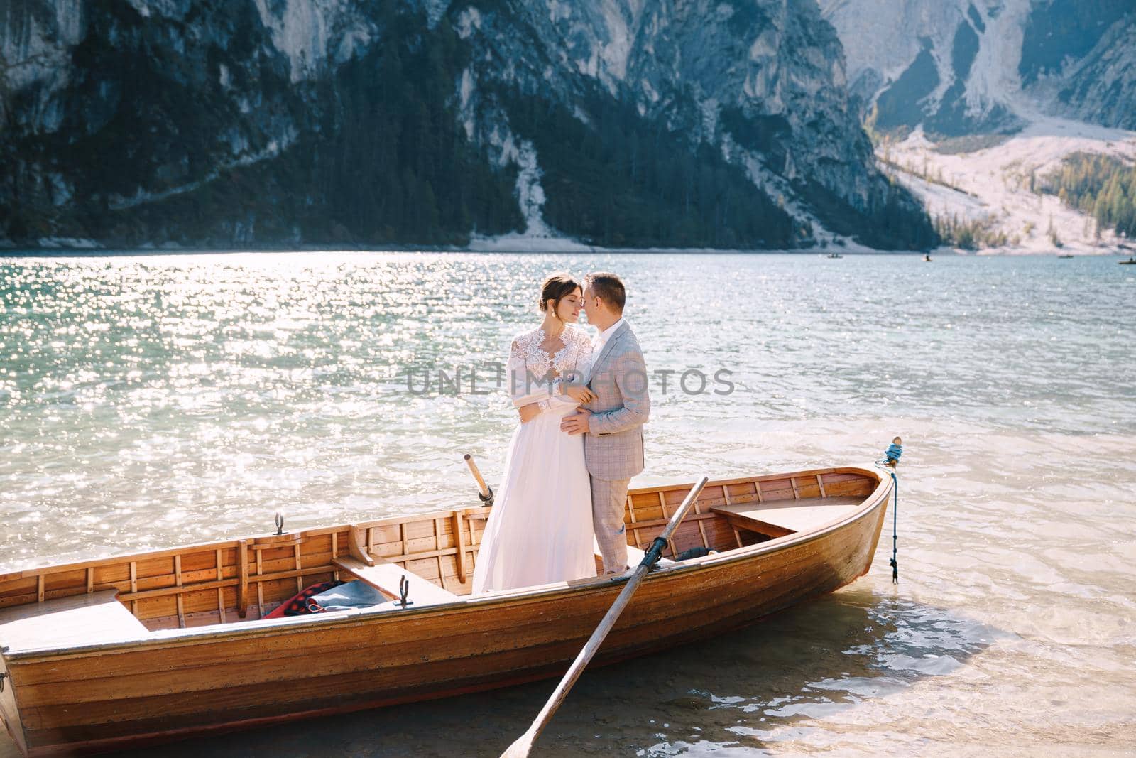 Bride and groom sailing in wooden boat, with oars at Lago di Braies lake in Italy. Wedding in Europe - Newlyweds are standing embracing in boat