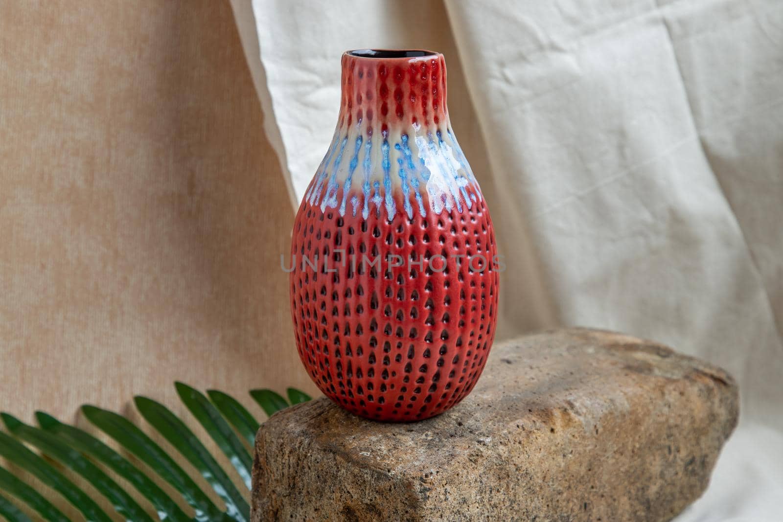 Red handmade ceramic vase on white textured table cloth.  Home decor, Copy space, Selective focus.