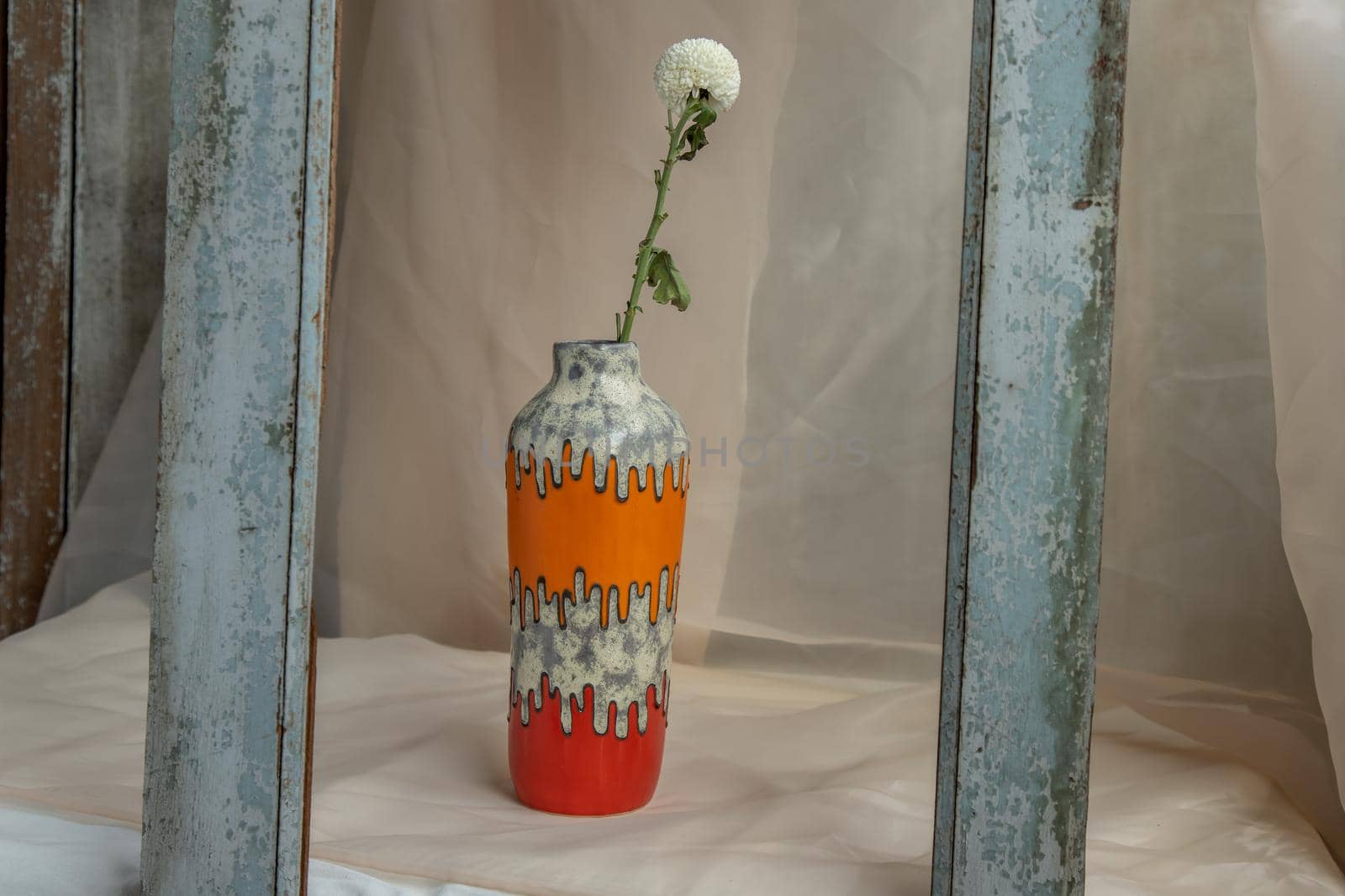 White flower in Orange and Red handmade ceramic vase on Blush textured table cloth. Home decor, Copy space, Selective focus.