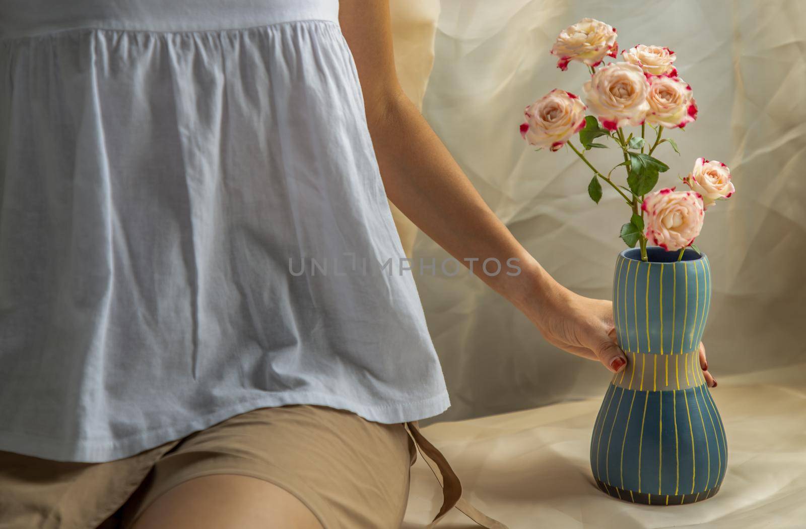 Hands of a young woman with Blue handmade ceramic vase and Bouquet of flower on Blush textured table cloth. Home decor, Copy space, Selective focus.