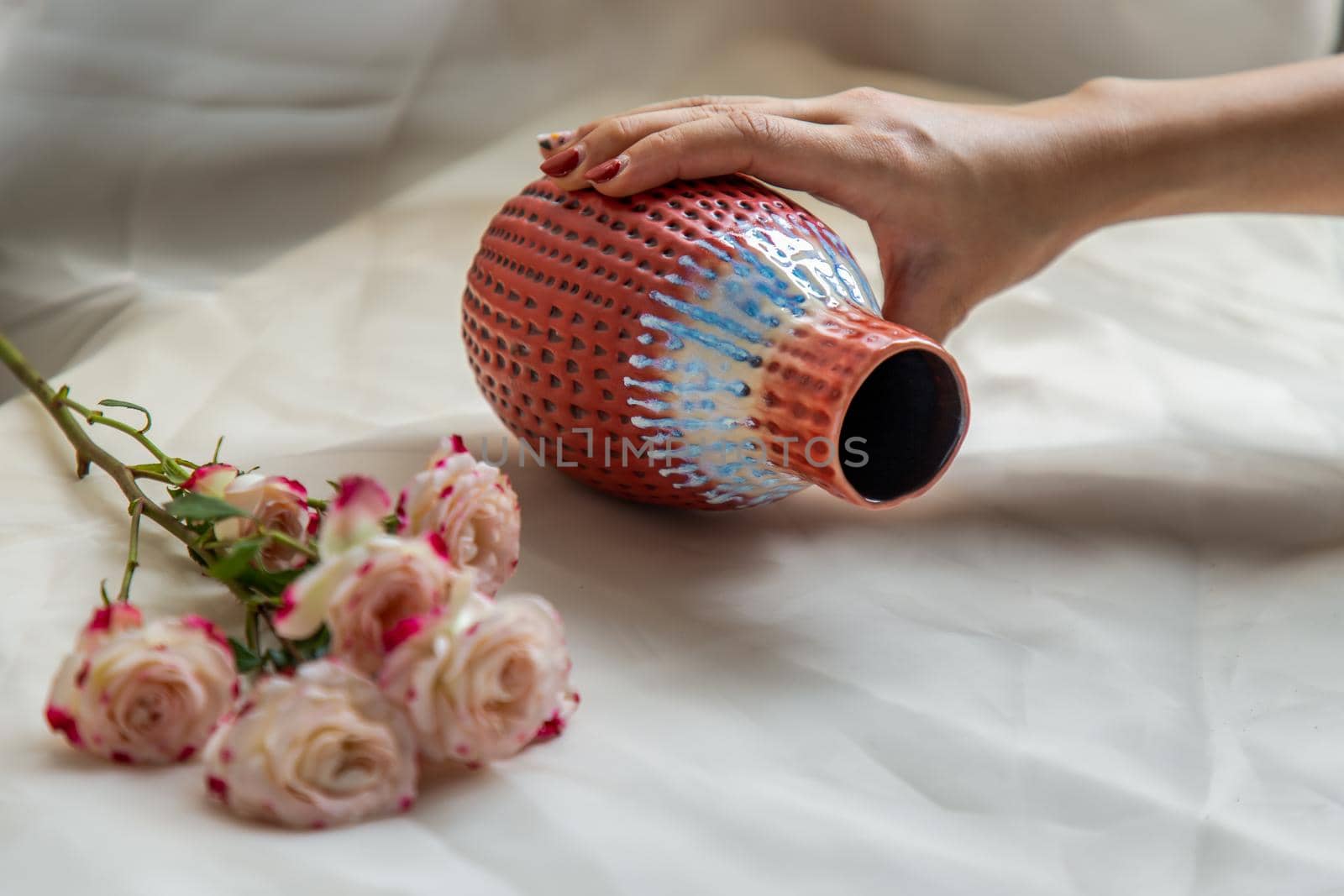 Hands of a young woman with Red vase and Bouquet of flowers on Blush textured table cloth. Home decor, Copy space, Selective focus.