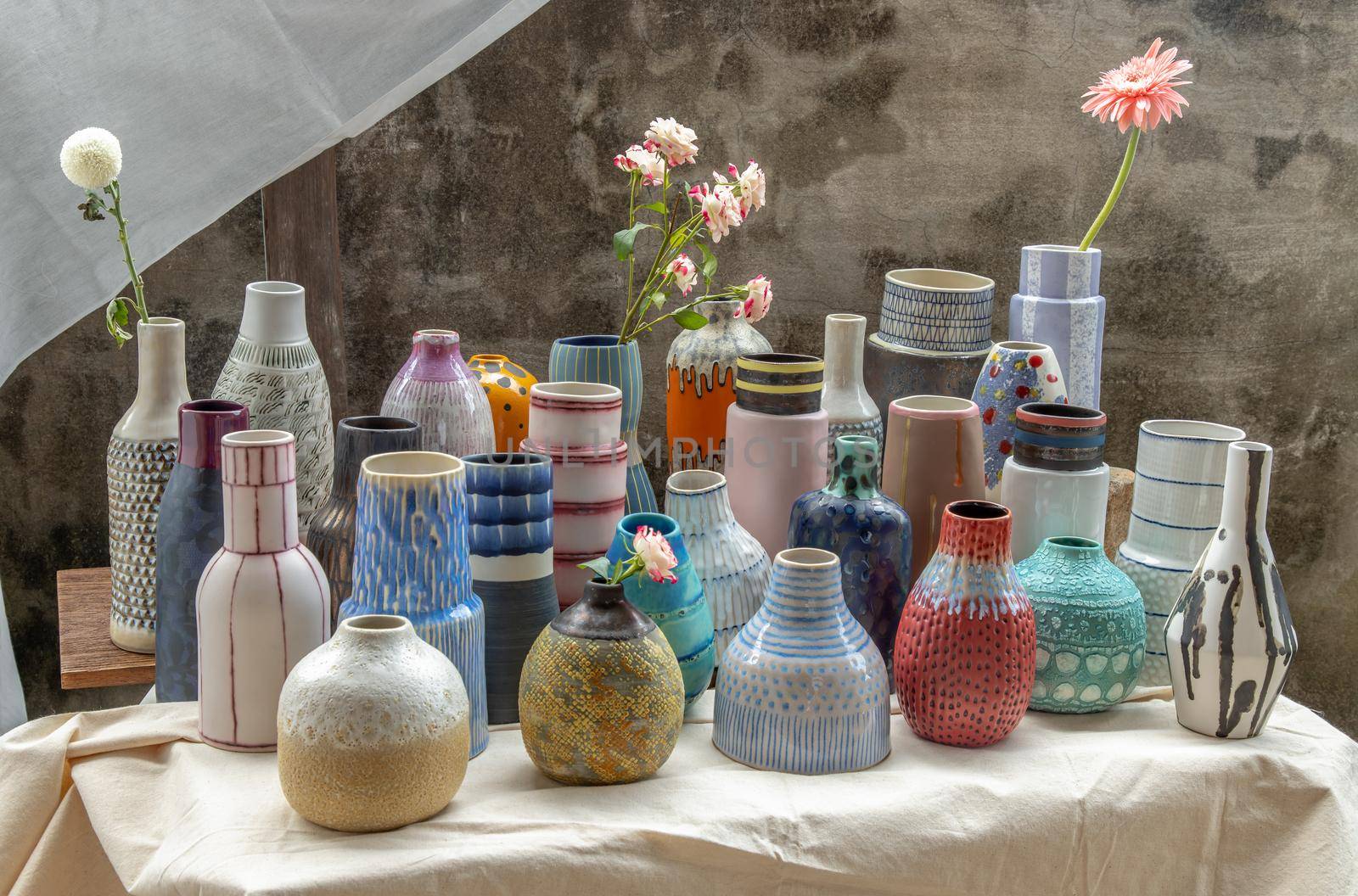 Bouquet of flowers in Handmade Assorted Many Different Ceramic Vases on Calico textured table cloth with old cement wall. Home decor. Selective focus.