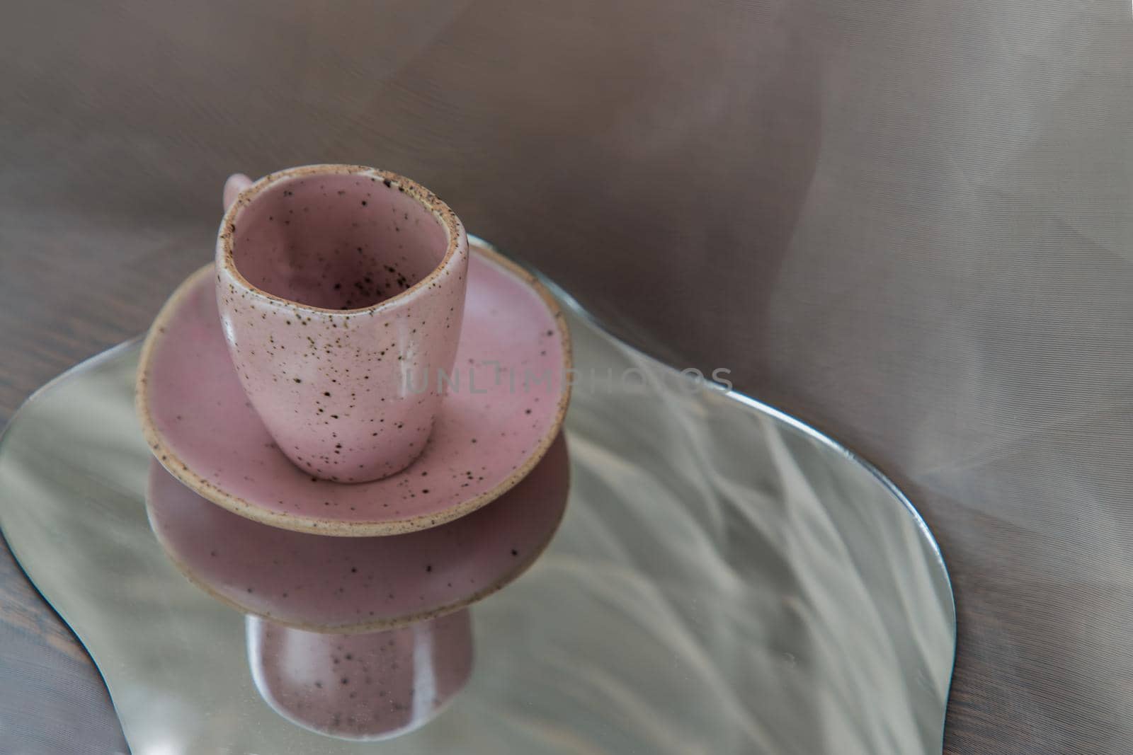 Pink handmade ceramic mug on mirror on fabric textured table cloth. Home decor, Copy space, Selective focus.