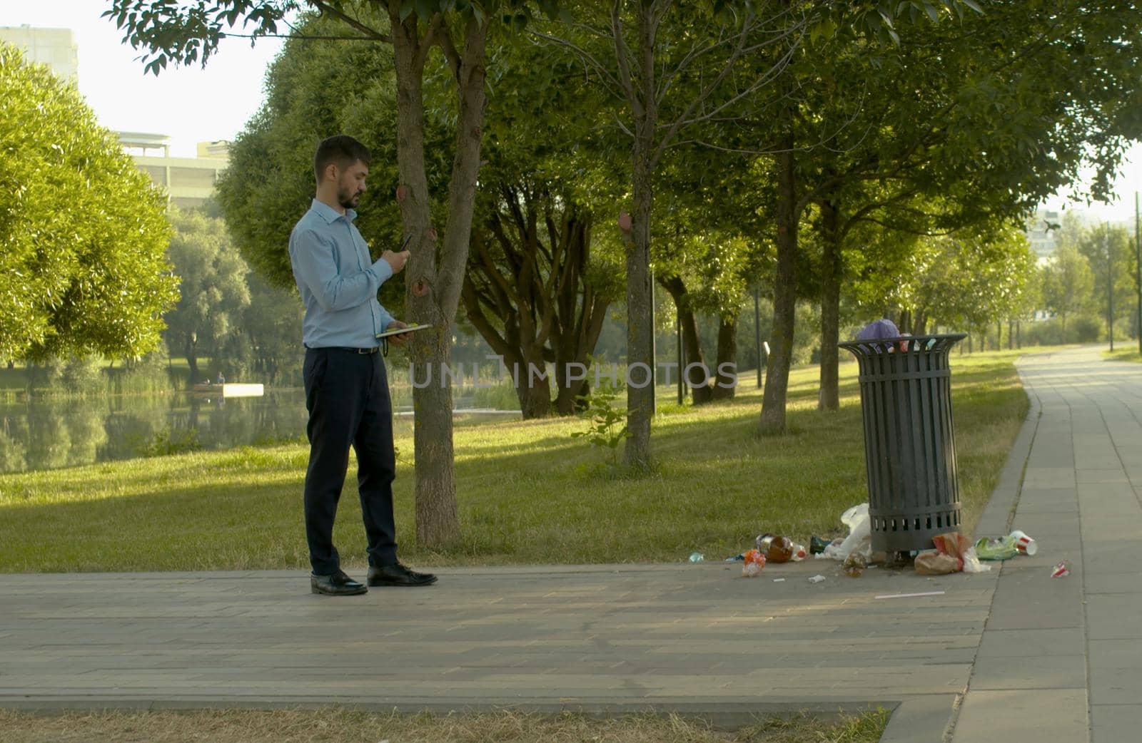Young inspector photographs the dirty trash can in the park
