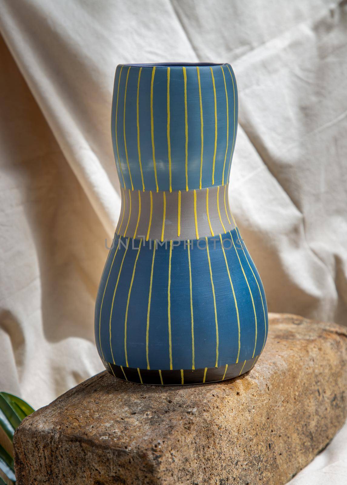 Blue and Yellow handmade ceramic vase on white textured table cloth.  Home decor, Copy space, Selective focus.