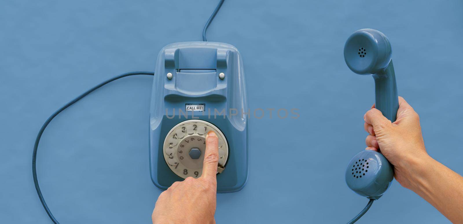 A blue vintage dial telephone handset with one hand and blue background. 