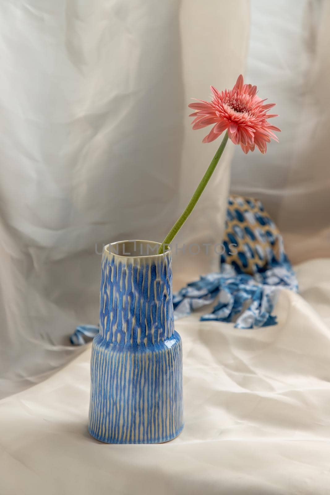 Pink flower in Blue handmade ceramic vase on Blush textured table cloth. Home decor, Copy space, Selective focus.