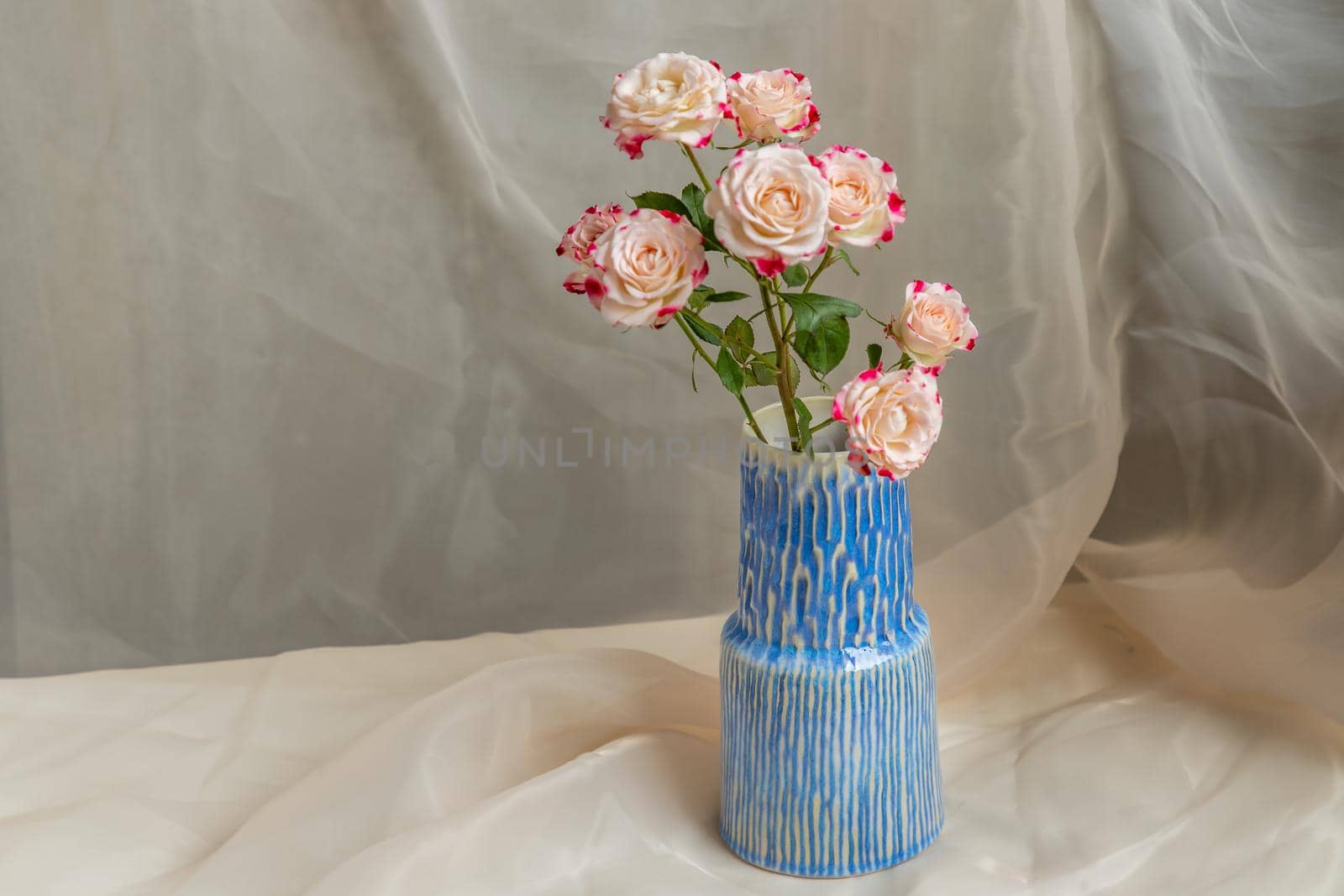 Bouquet of flower in Blue handmade ceramic vase on Blush textured table cloth. Home decor, Copy space, Selective focus.