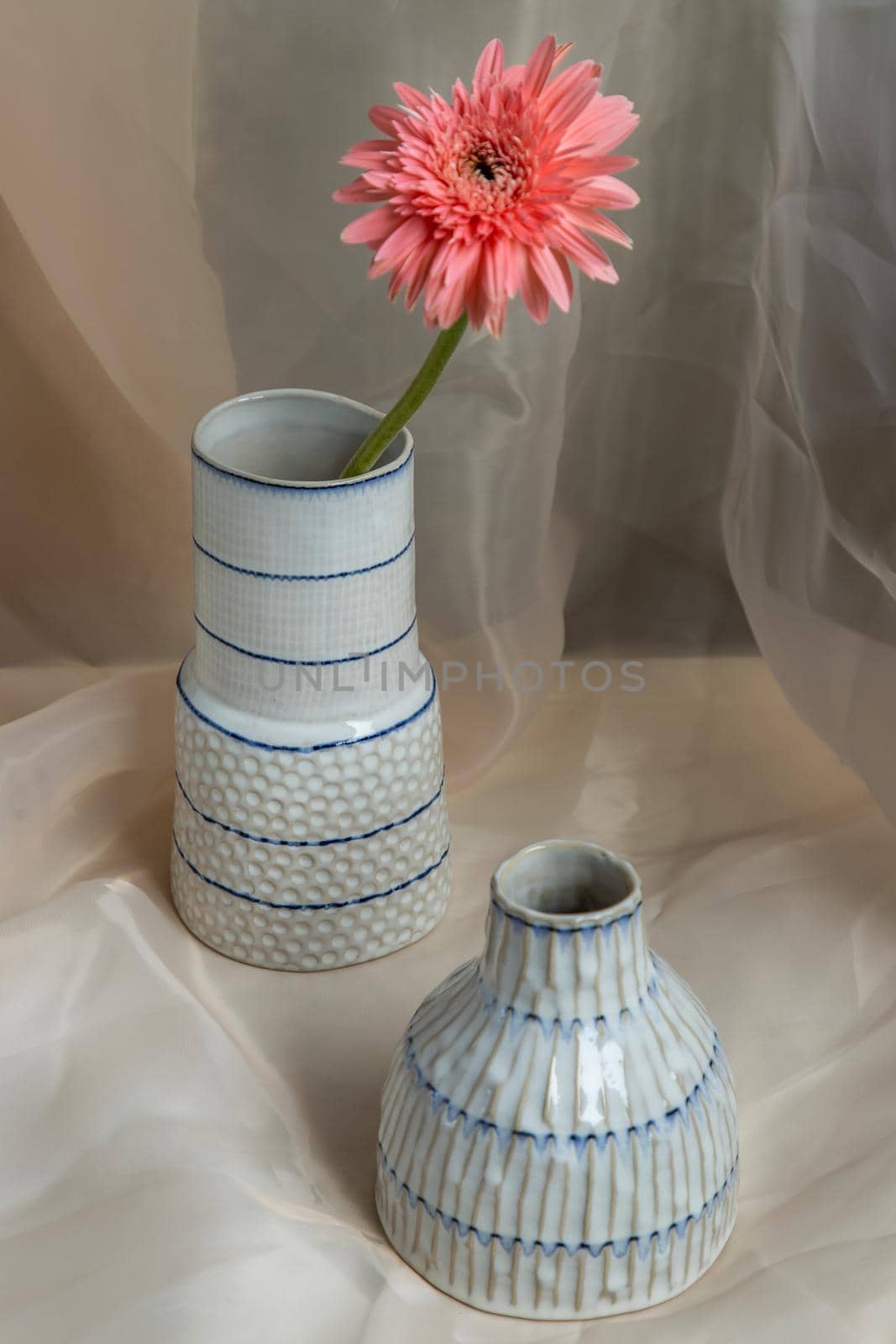 Pink flower in White and Blue handmade ceramic vases on Blush textured table cloth. Home decor, Copy space, Selective focus.