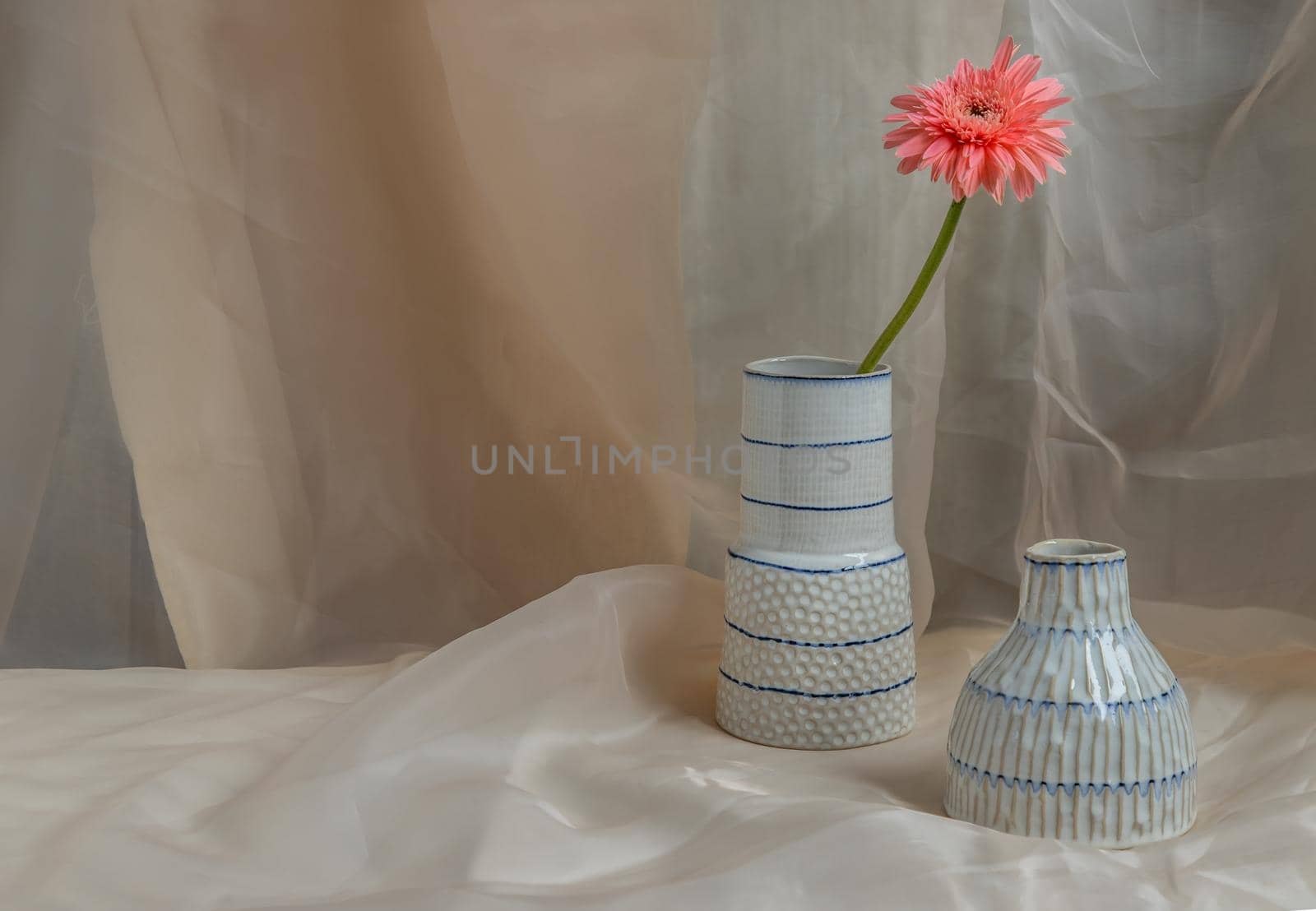 Pink flower in White and Blue handmade ceramic vases on Blush textured table cloth. Home decor, Copy space, Selective focus.