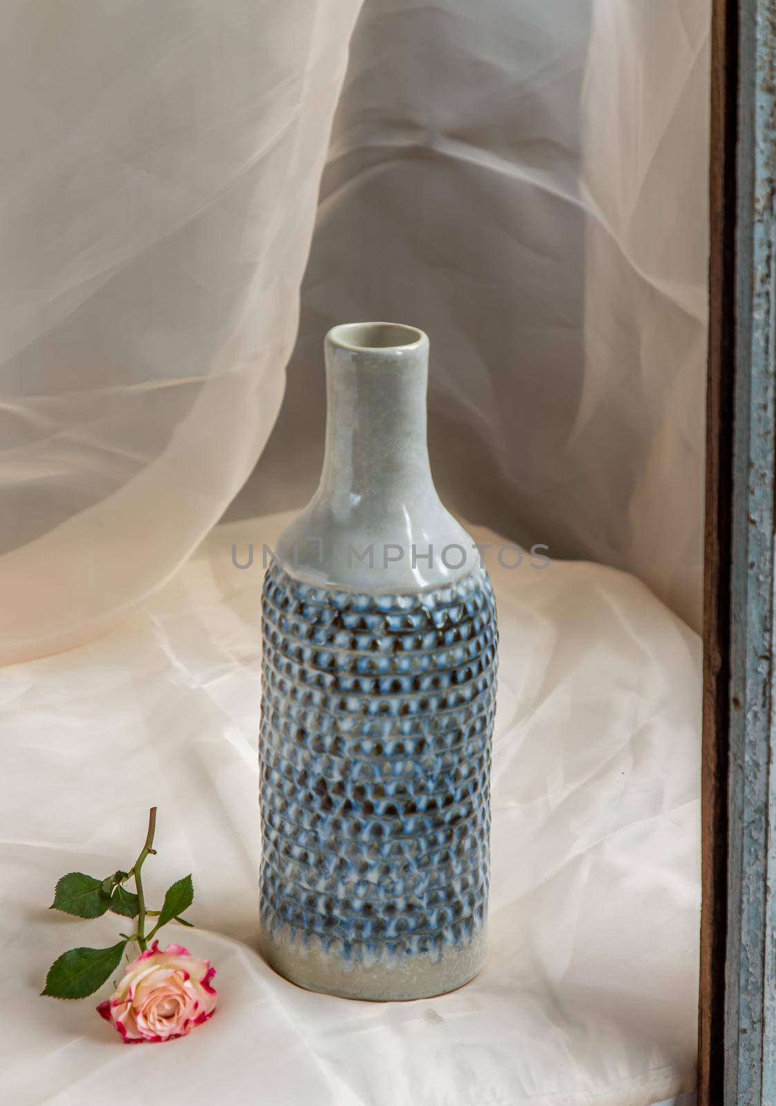 Blue handmade ceramic vase with flower on Blush textured table cloth.  Home decor, Copy space, Selective focus.